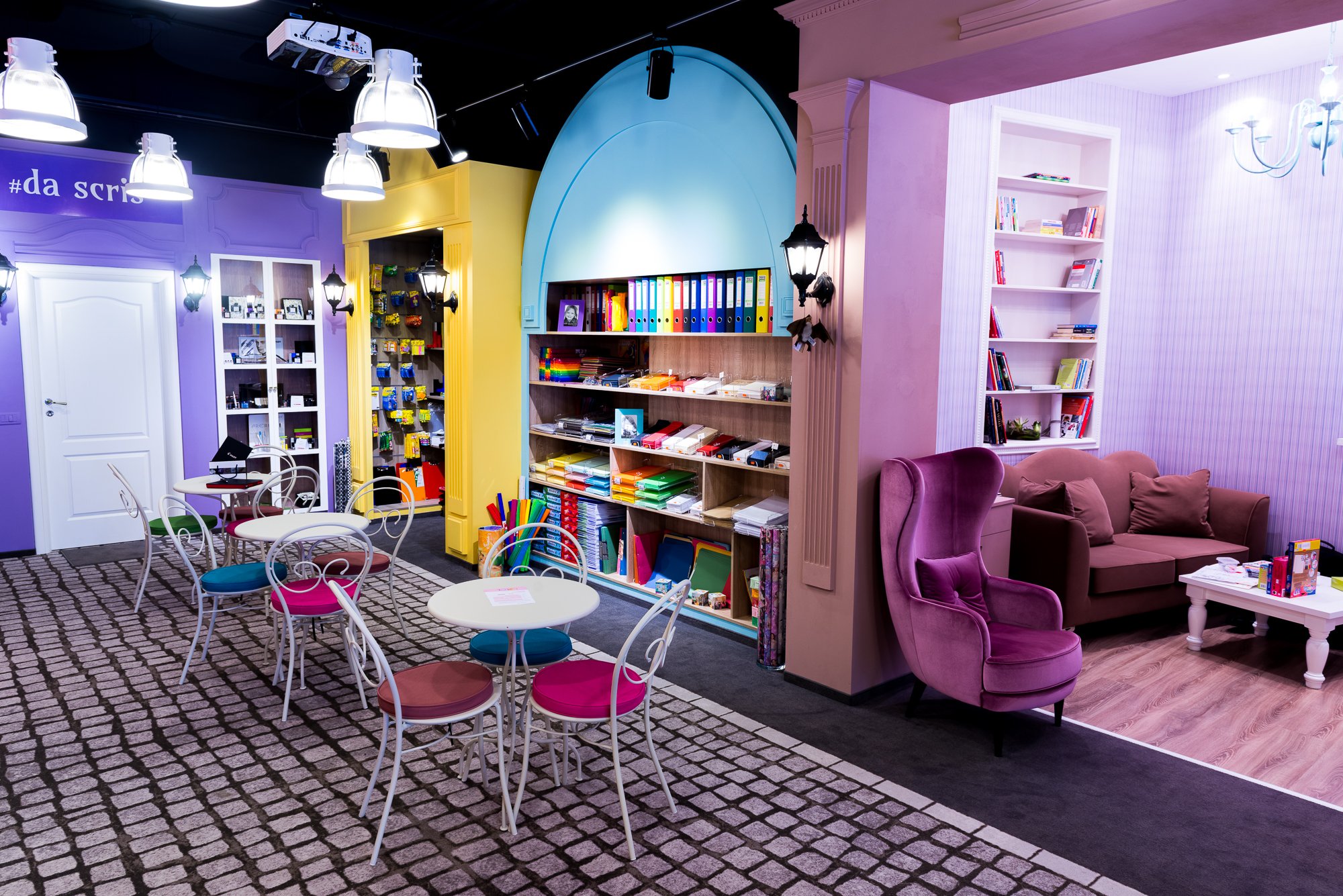 Colorful interior of a room with purple, yellow, and pink walls, featuring bookshelves, tables, and chairs.