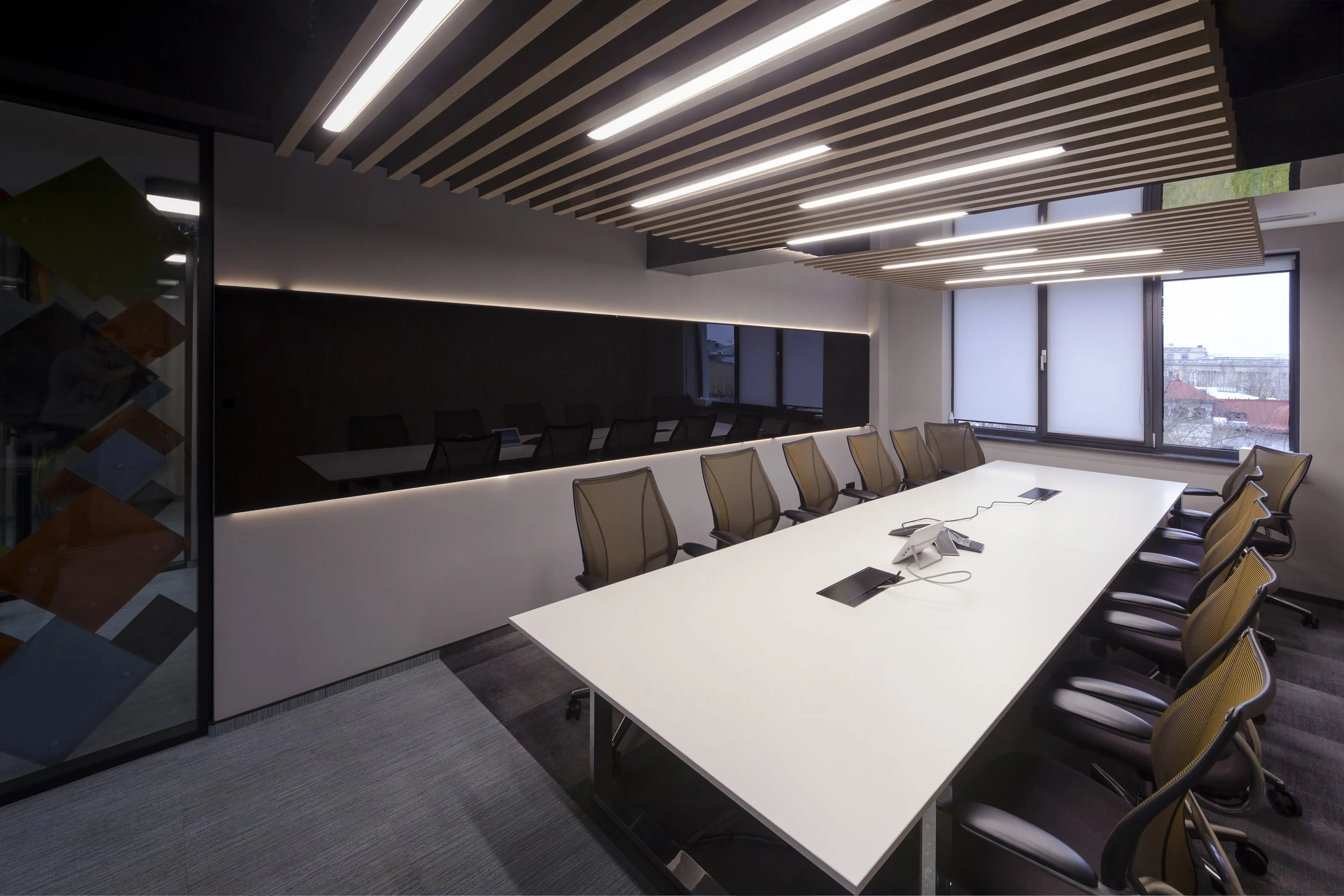 Empty modern conference room with large white table, mesh office chairs, and large windows with blinds.