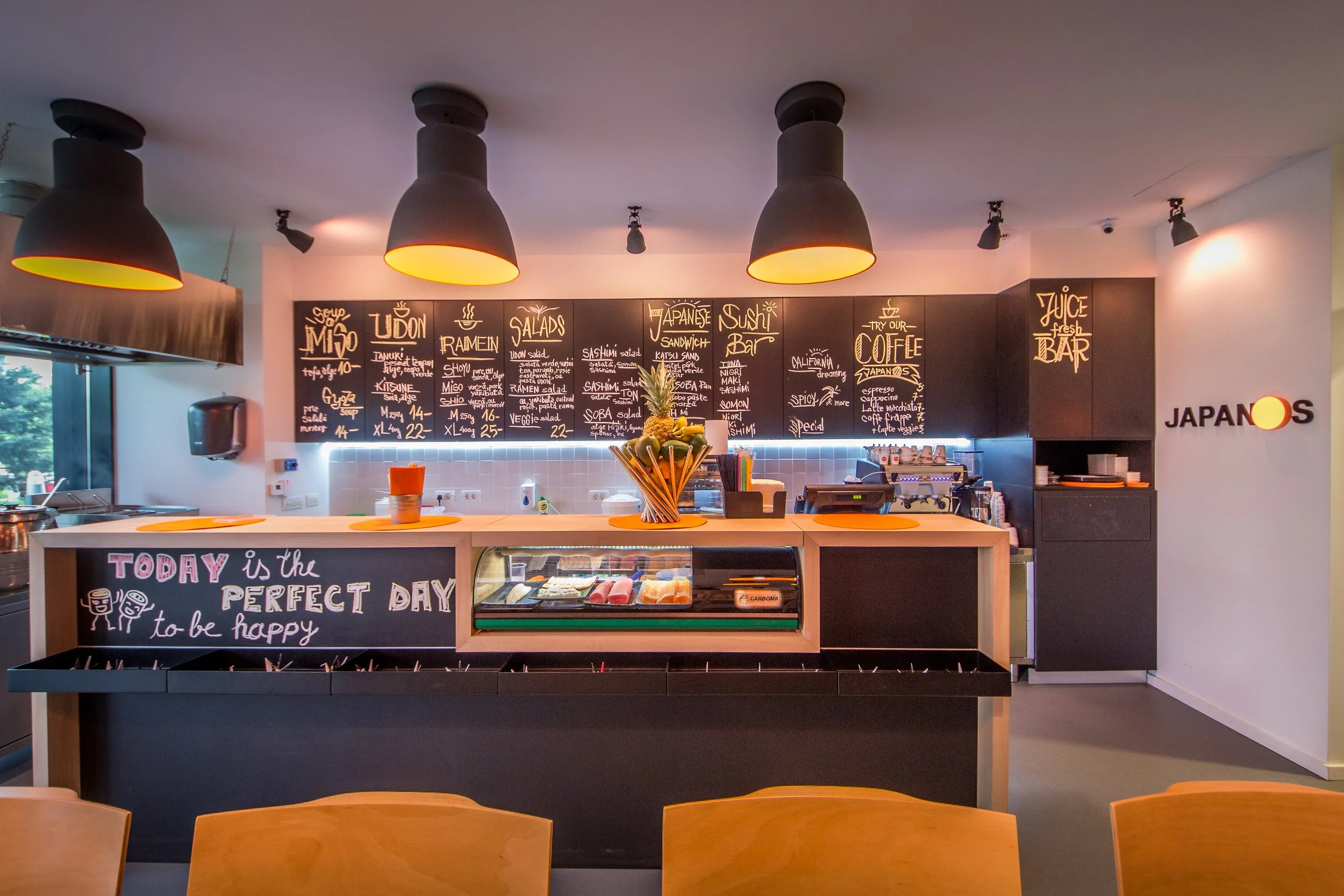 Interior of a modern Japanese restaurant with a chalkboard menu, sushi bar, and orange accents.