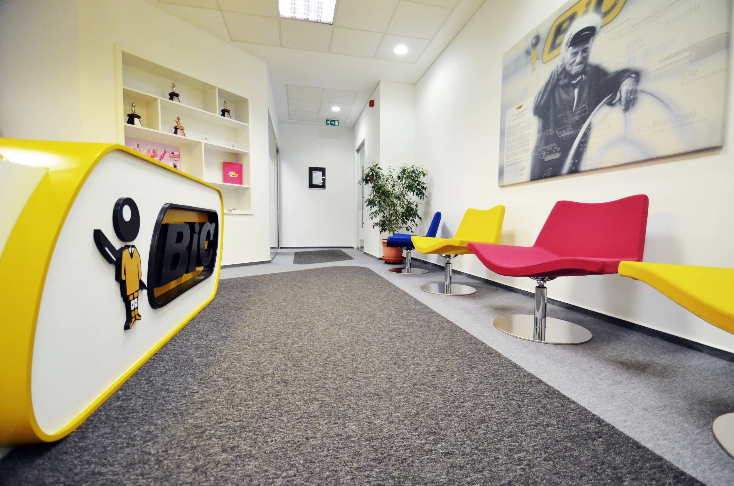 Waiting area with colorful chairs, a potted plant, and a hallway in a modern office or clinic.