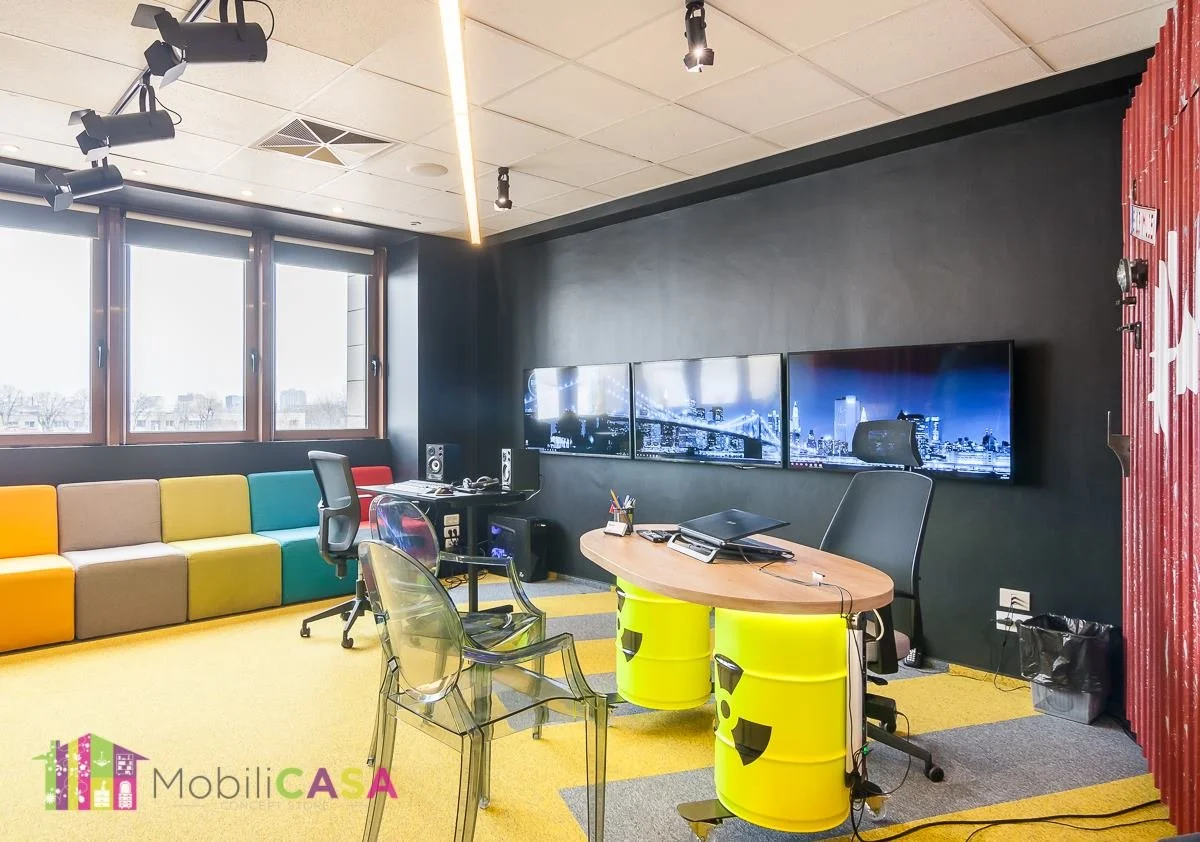 Modern office or creative workspace with black walls, large windows, colorful bench seating, a desk with bright yellow barrel seats, and multiple screens showing cityscape images.