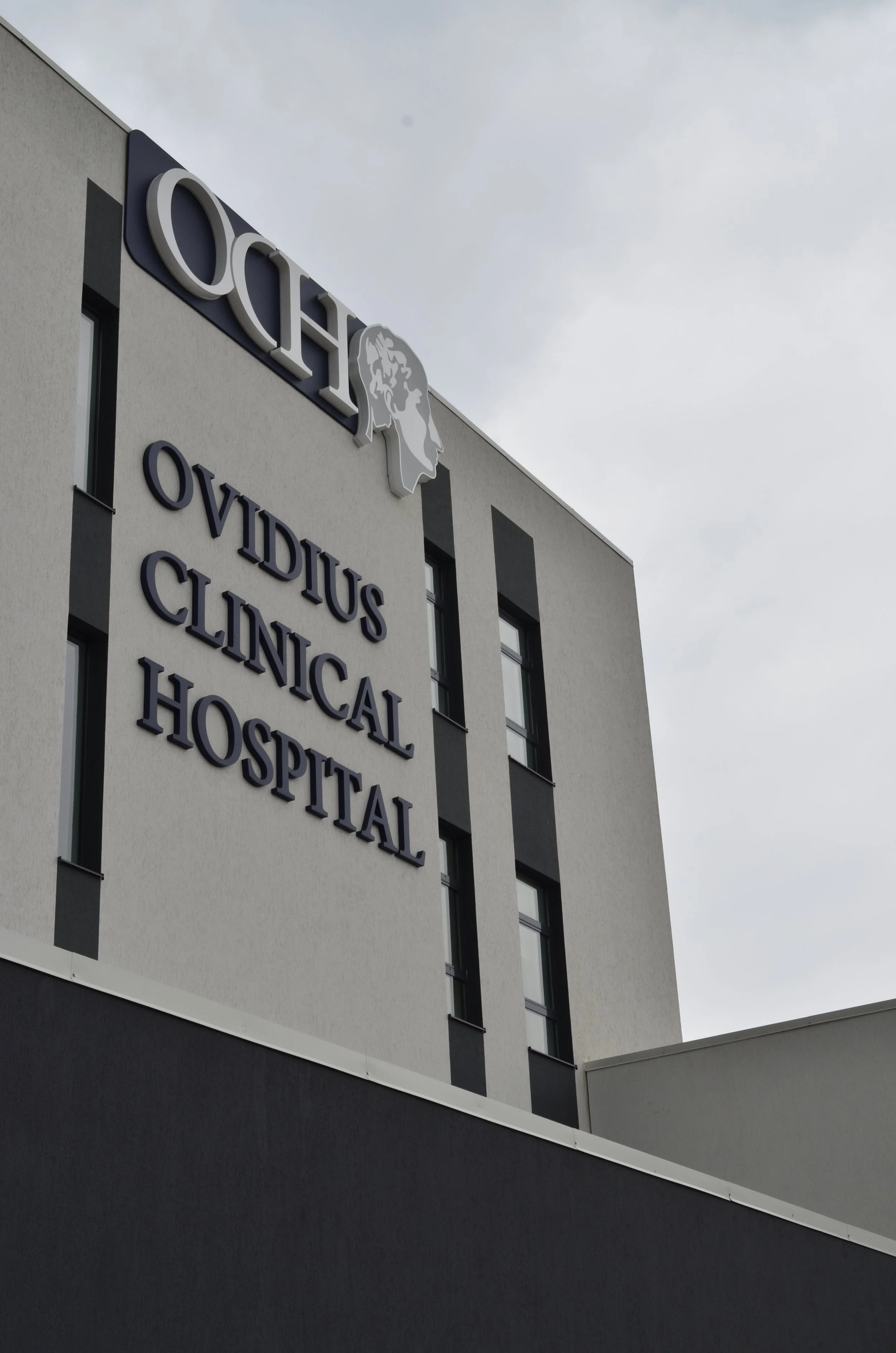 Exterior of a building with a sign that reads 'OCH OVIDIUS CLINICAL HOSPITAL' and a logo of a female profile with a lion's head.