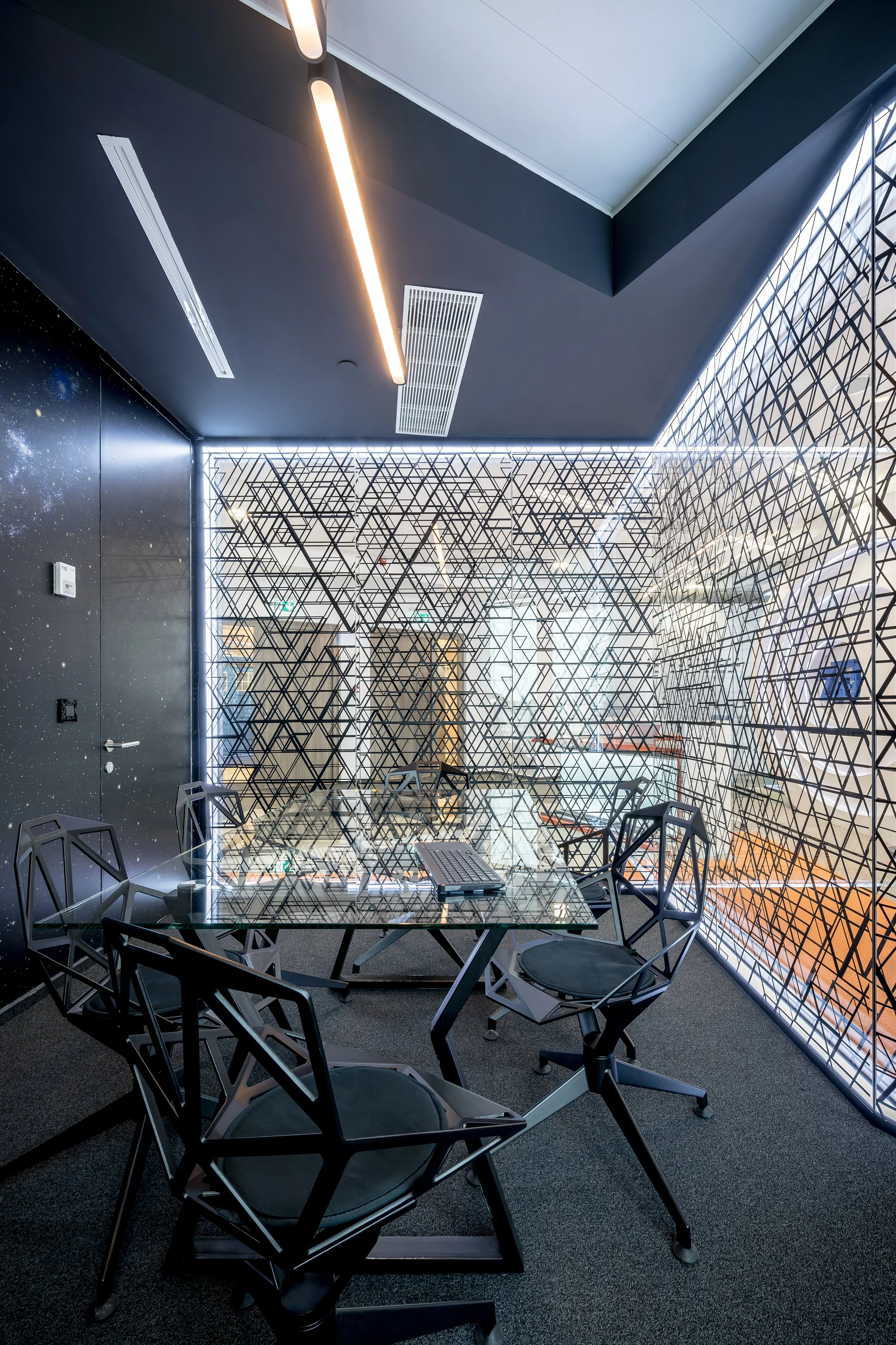 Modern conference room with a glass table, black chairs, and geometric-patterned glass walls illuminated with thin LED lights.