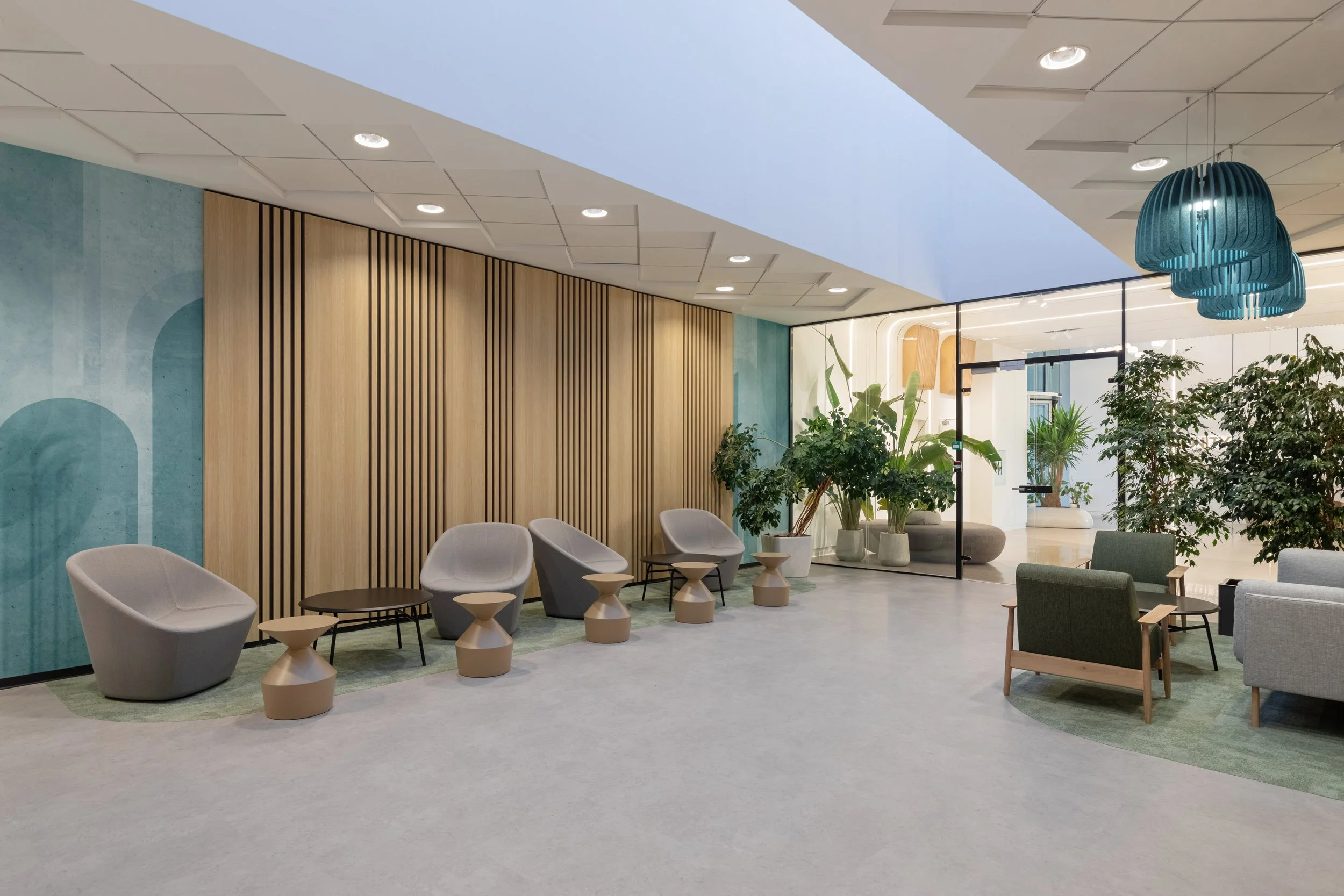 Modern interior lounge area with contemporary chairs, small tables, green potted plants, and colorful ceiling lighting.