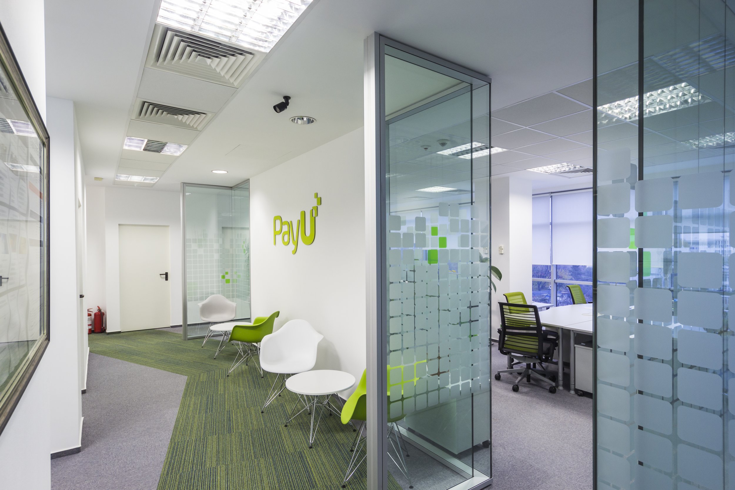 Modern office space with a waiting area with white and green chairs, glass walls, and the PayU logo on the wall.