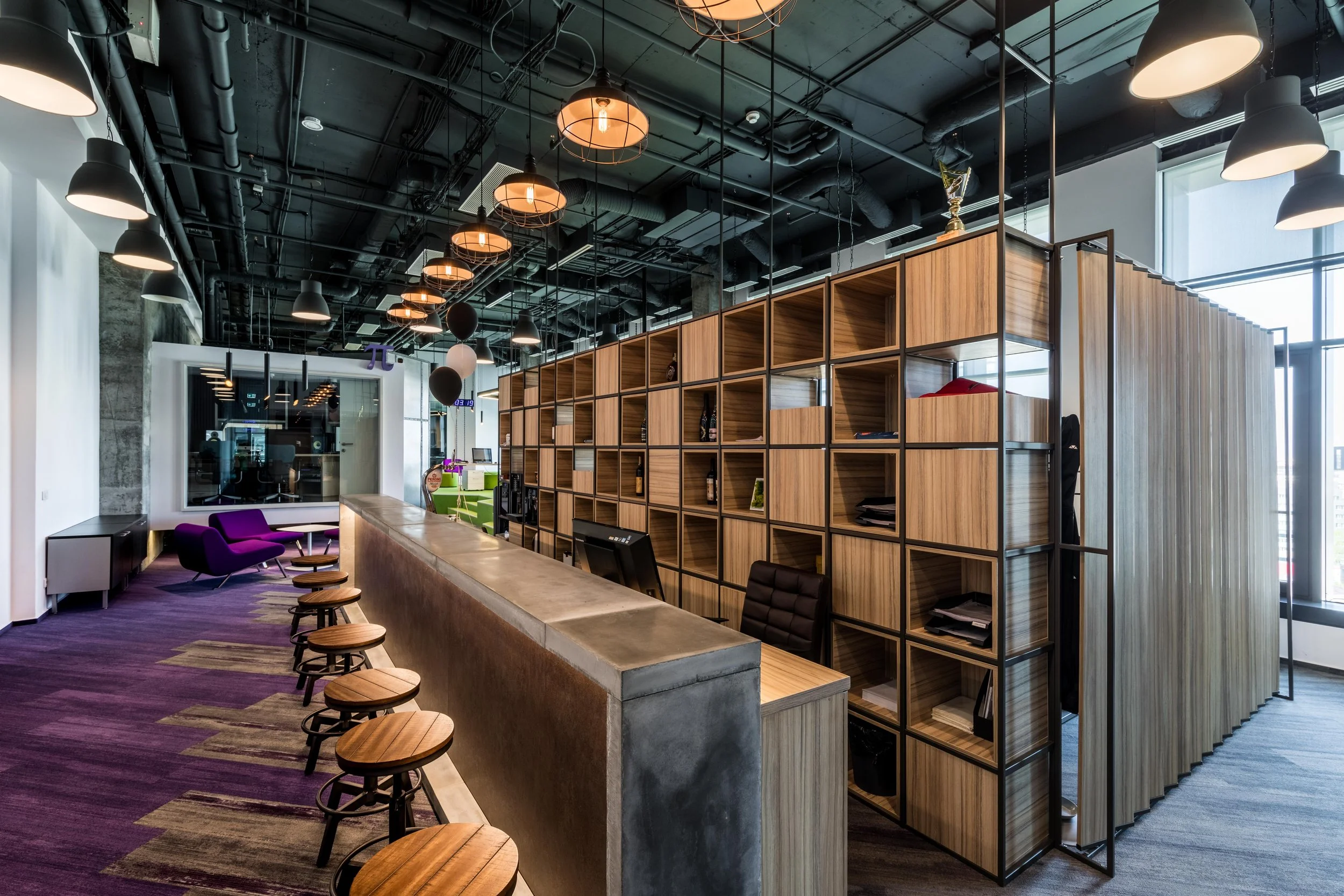 Modern office reception area with purple chairs, wooden shelving, and pendant lighting fixtures.