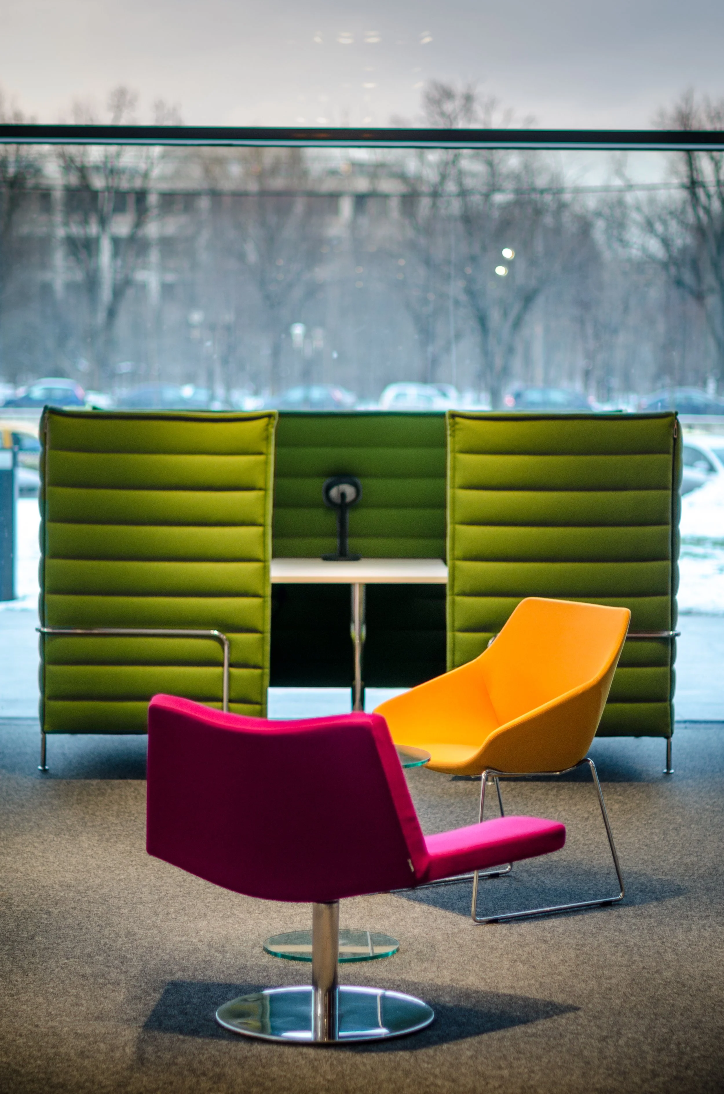 Colorful modern chairs inside an office with a large window showing trees and parked cars outside.