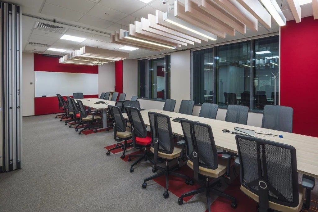 Empty office conference room with a long table and black chairs, large windows, and modern ceiling lighting.