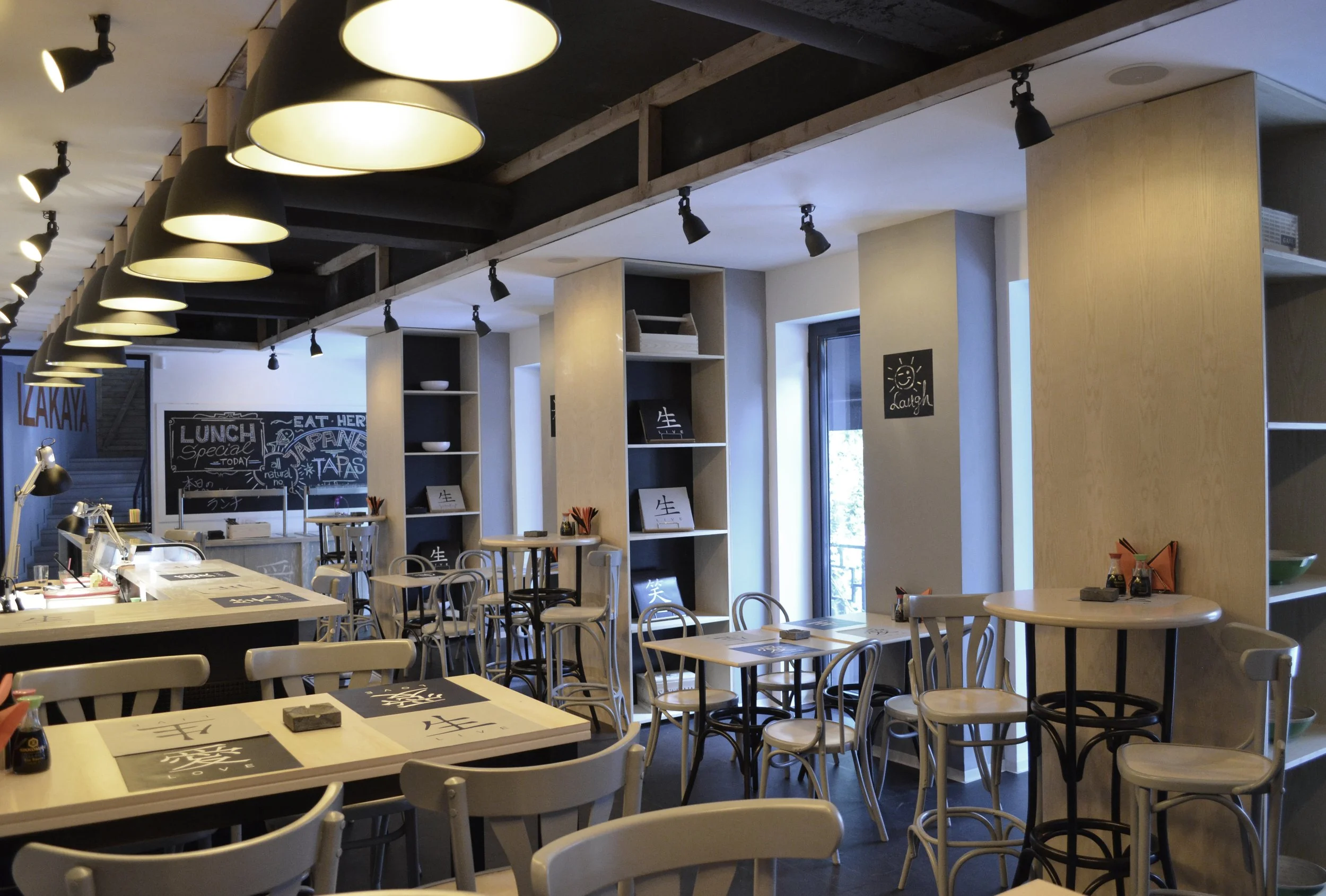 Interior of a modern restaurant with white and black furniture, pendant and track lighting, and chalkboard menus on the walls.