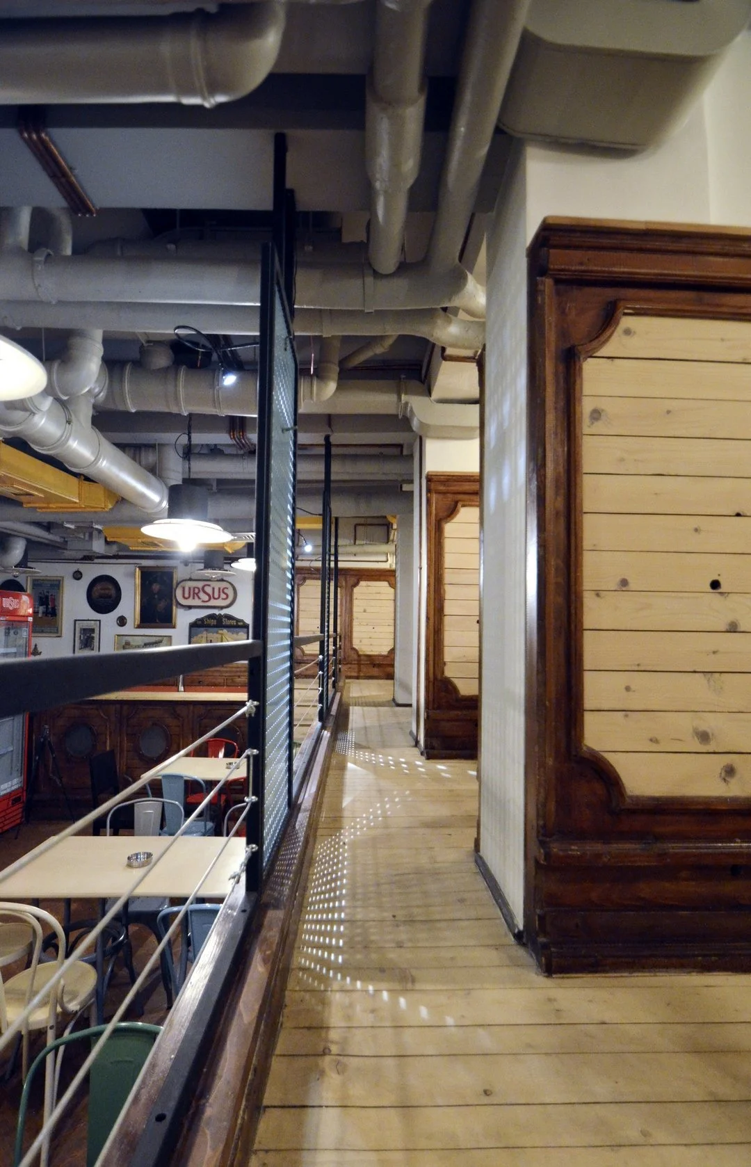 Wooden flooring and paneling in a restaurant or cafe with visible ceiling pipes and industrial decor elements.