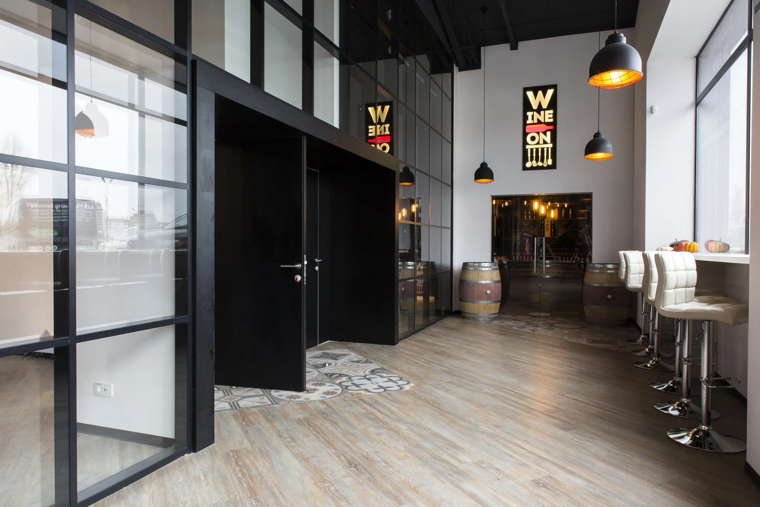 Interior of a modern bar or cafe with large window, black and white decor, pendant lights, bar stools, and decorative pumpkins on the windowsill.