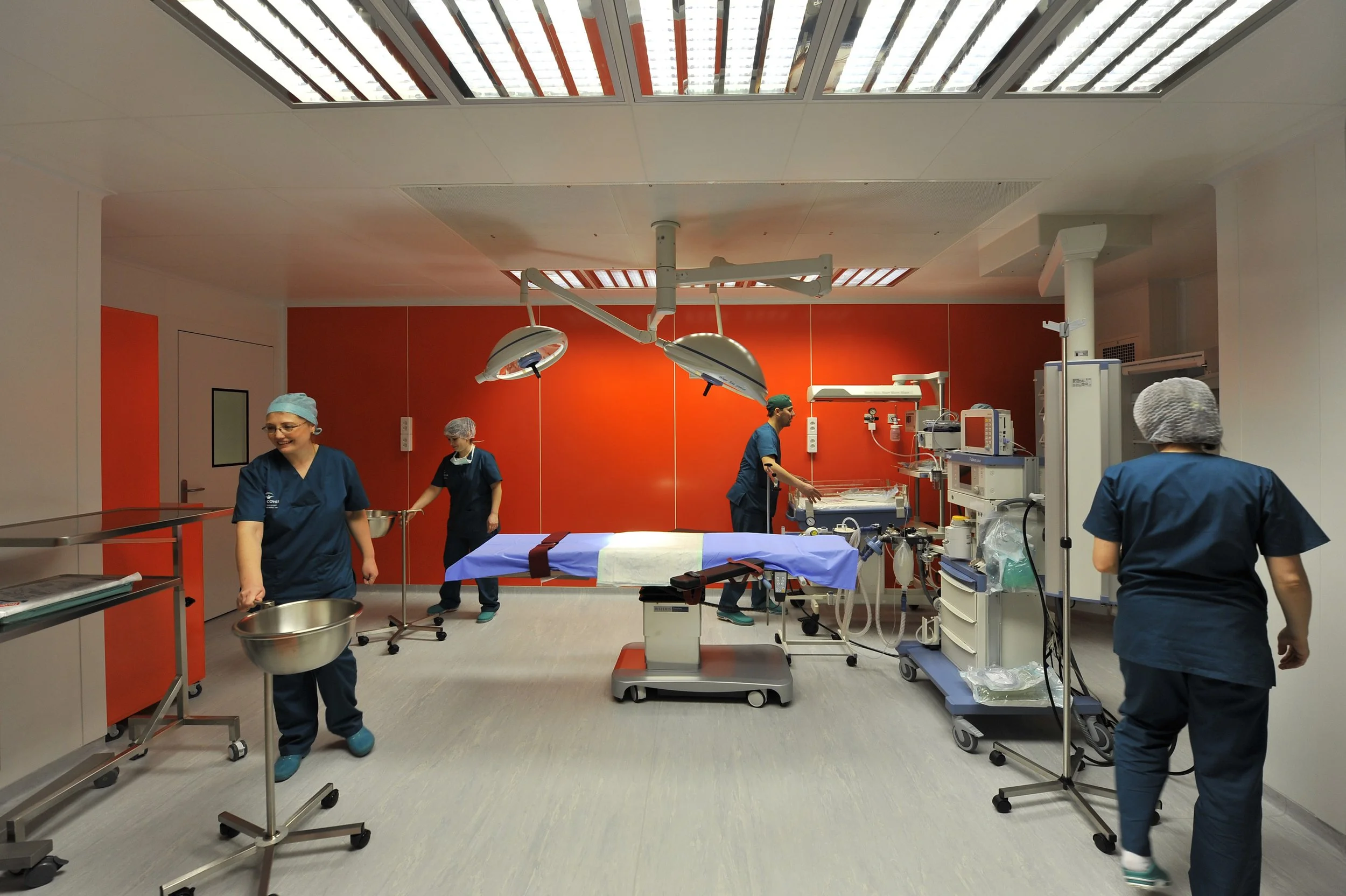 Operating room with medical staff preparing for surgery, featuring surgical tables, lights, and medical equipment.