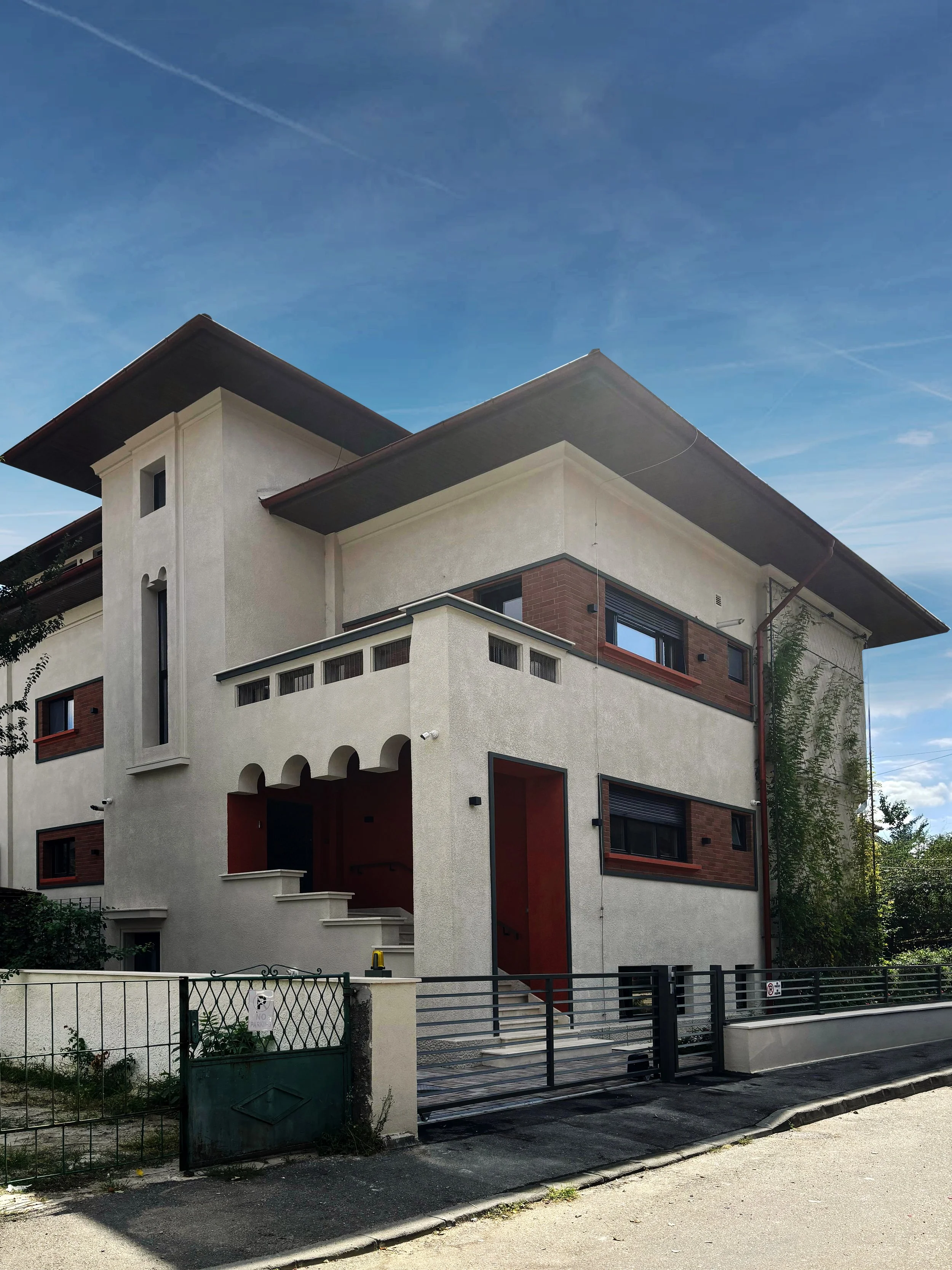 Modern multi-story house with white stucco walls, brick accents, and metal railings, set against a blue sky.