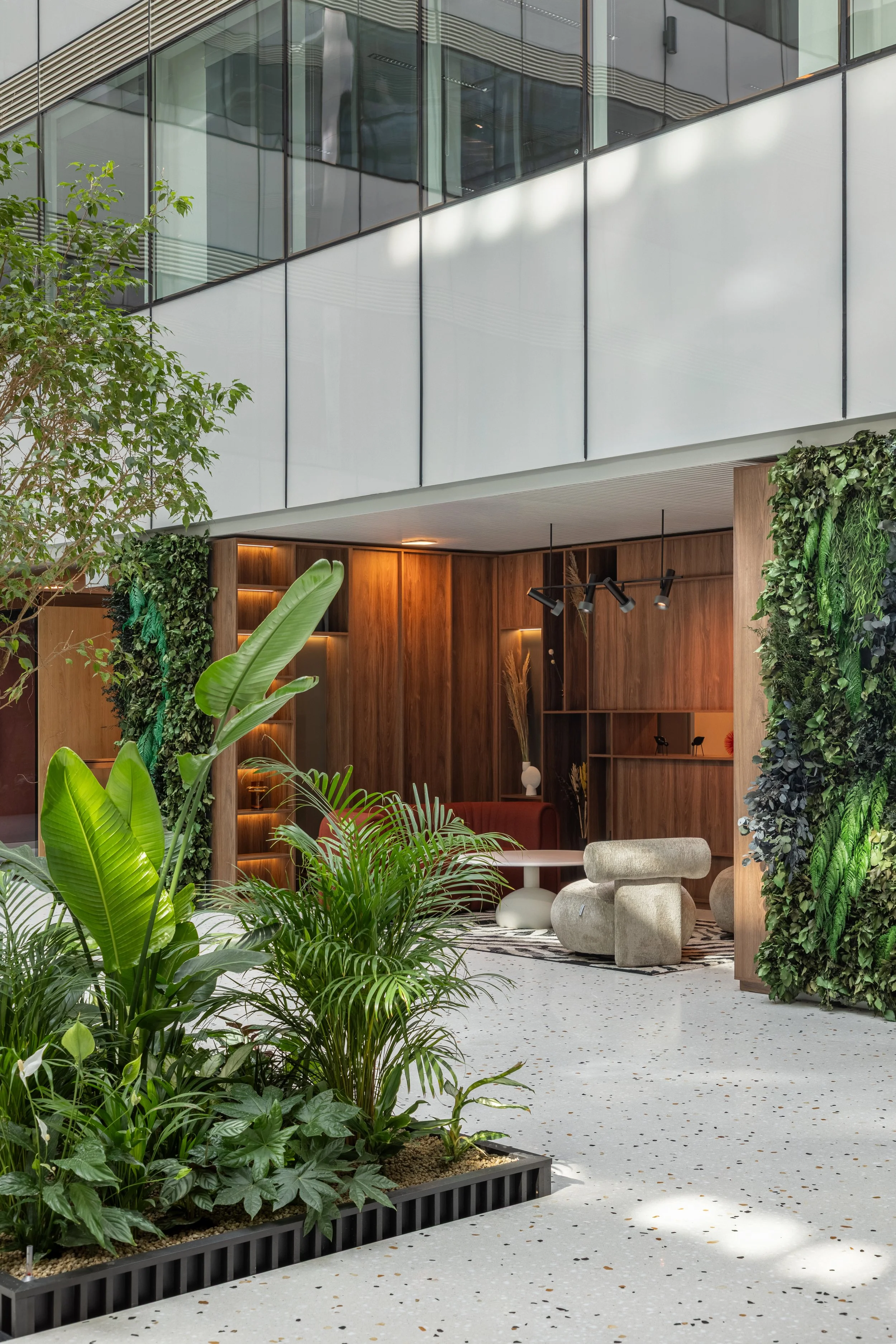Modern indoor lobby or lounge area with lush green plants, wood paneling, and contemporary furniture.