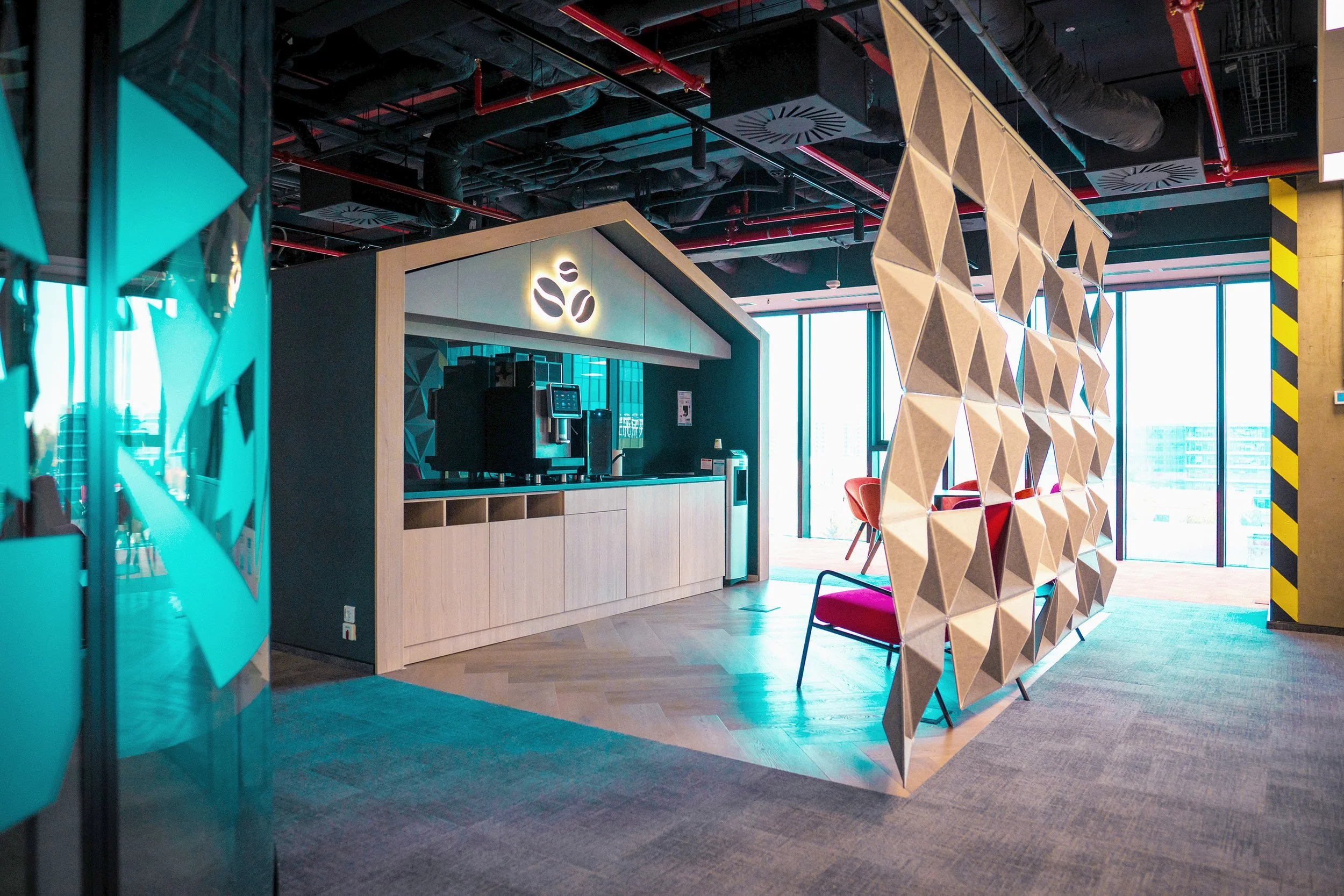 Modern office lounge with a coffee station, a colorful lattice room divider, and large windows letting in natural light.