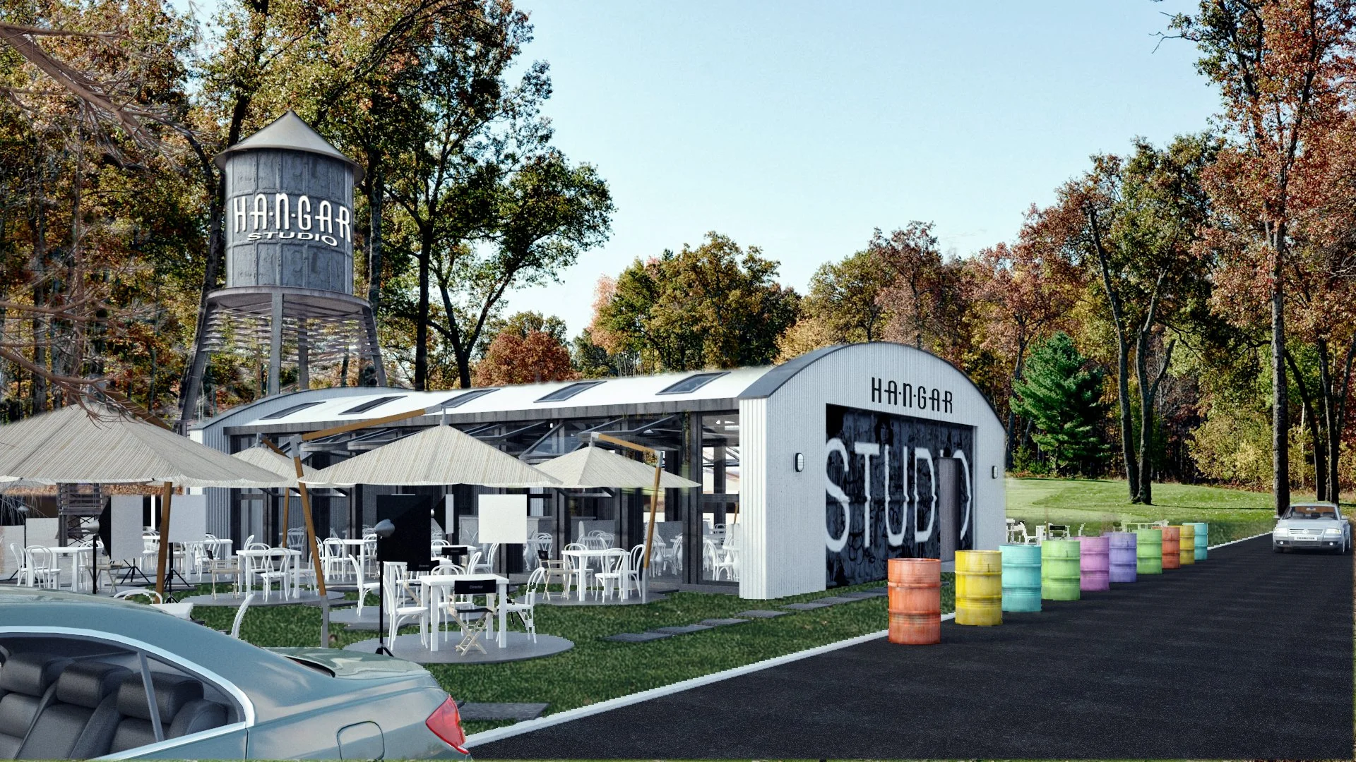 An outdoor scene featuring a modern hangar with a sign reading 'HANGAR STUDIOS,' surrounded by parking lot and trees with fall foliage. There are colorful barrels lined up outside and patio tables with umbrellas.