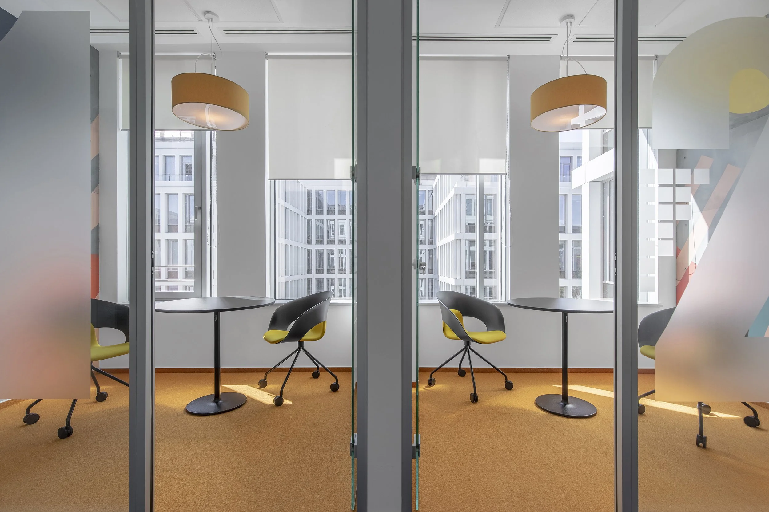 Modern office meeting rooms with glass walls, black tables, black and yellow chairs, orange carpet, large windows, and round ceiling lights.