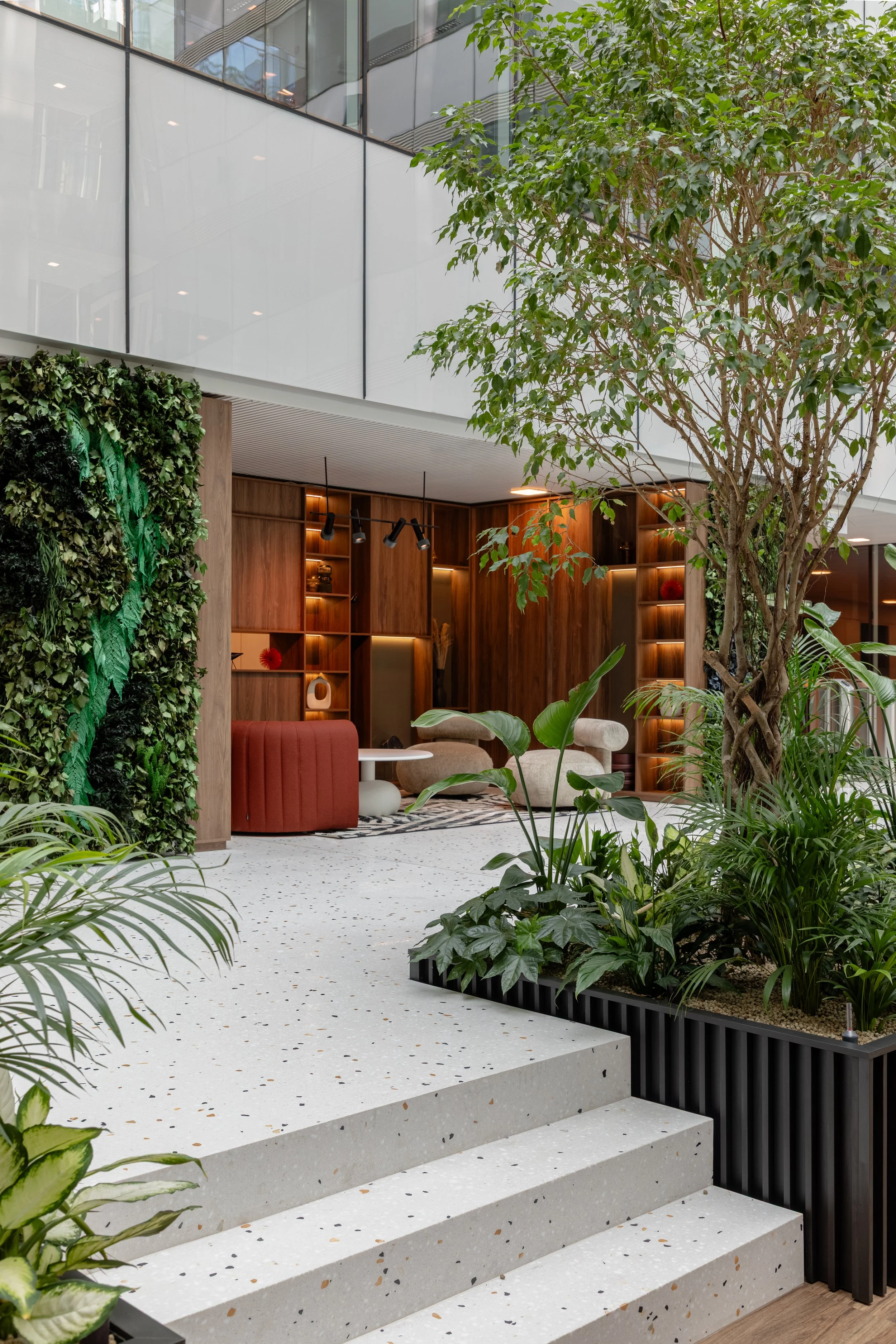 Interior of a modern space with terrazzo flooring, lush greenery, and a wooden wall with decorative shelves, lit by spotlights and natural light.