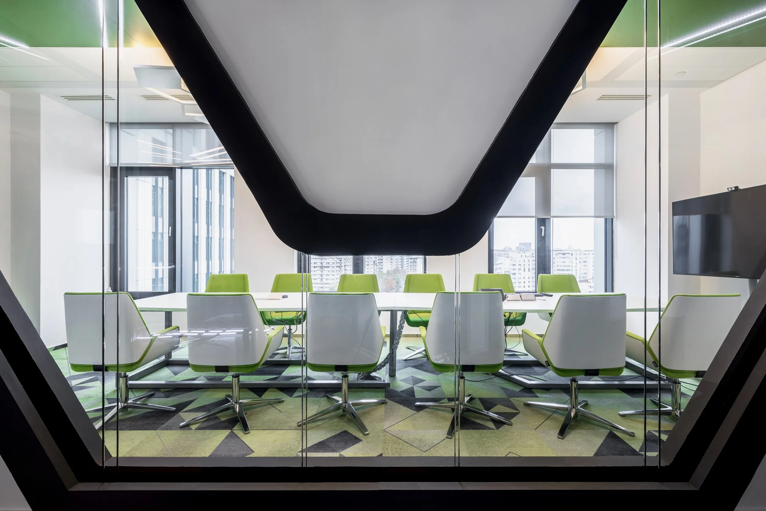 Modern conference room with white and green chairs, glass walls, large windows, and a cityscape view.
