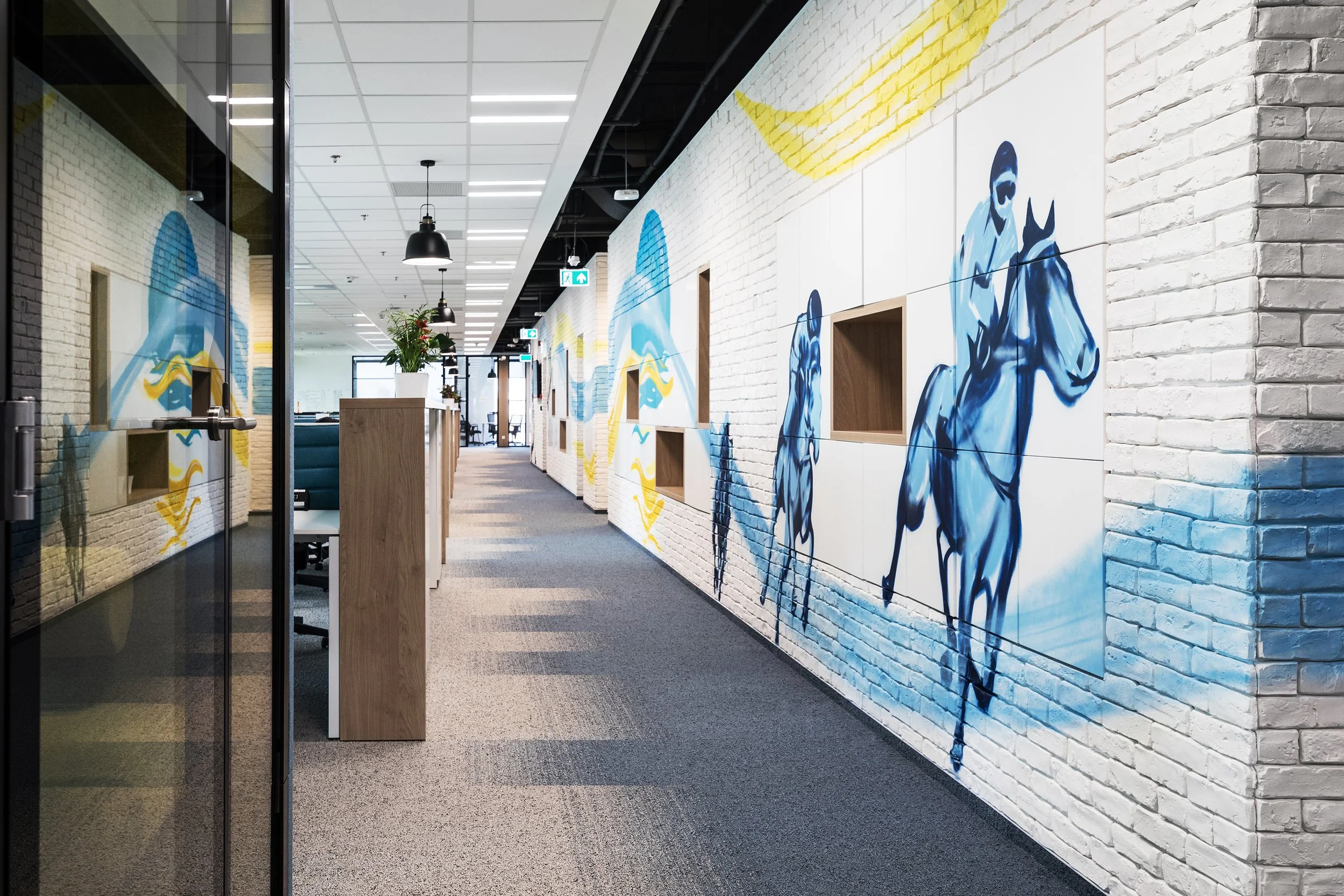 Interior hallway of an office with white brick walls featuring blue and yellow mural of horses and people.