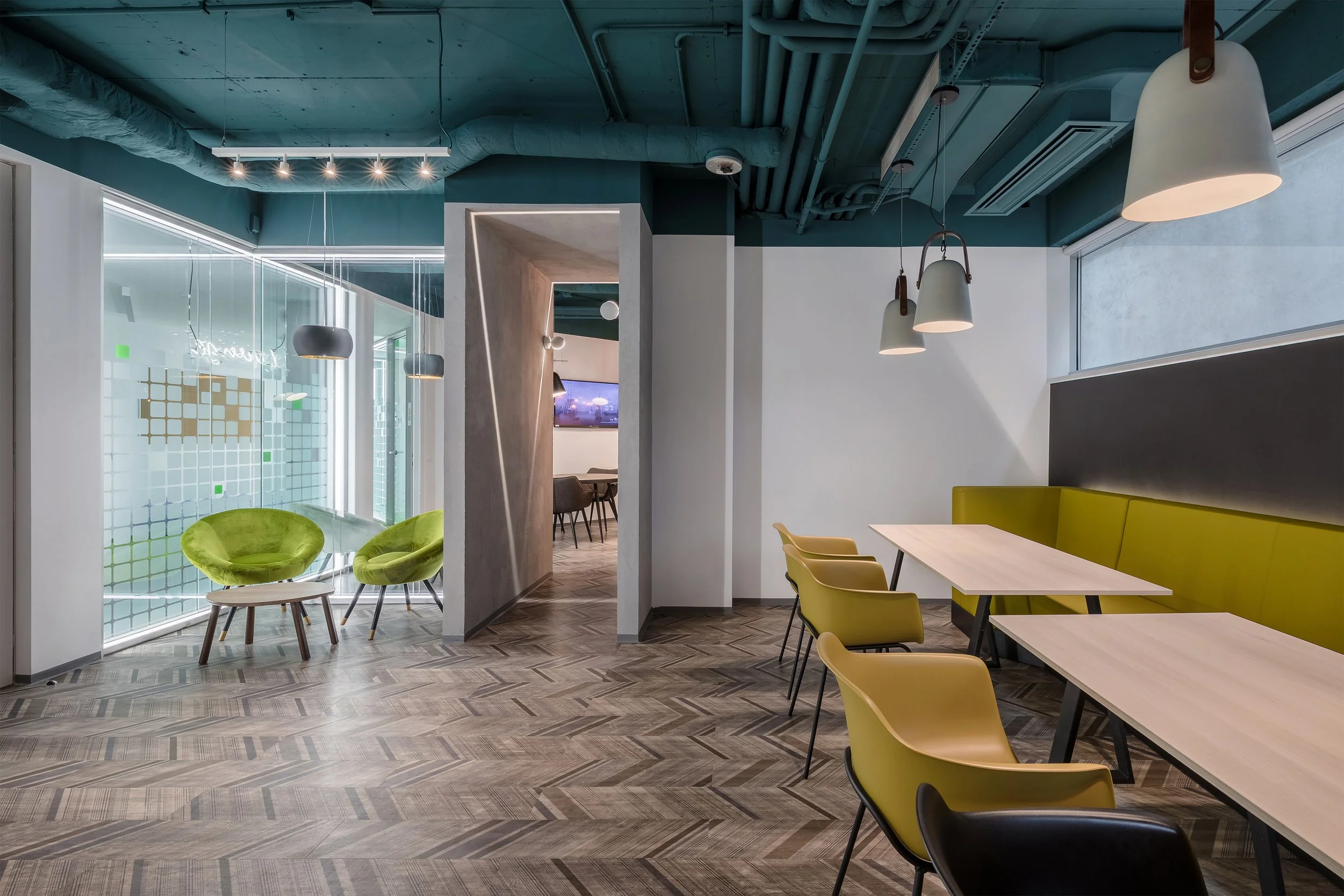 Modern office lounge and meeting area with yellow and black chairs, green cushioned seating, tables, and contemporary lighting fixtures.