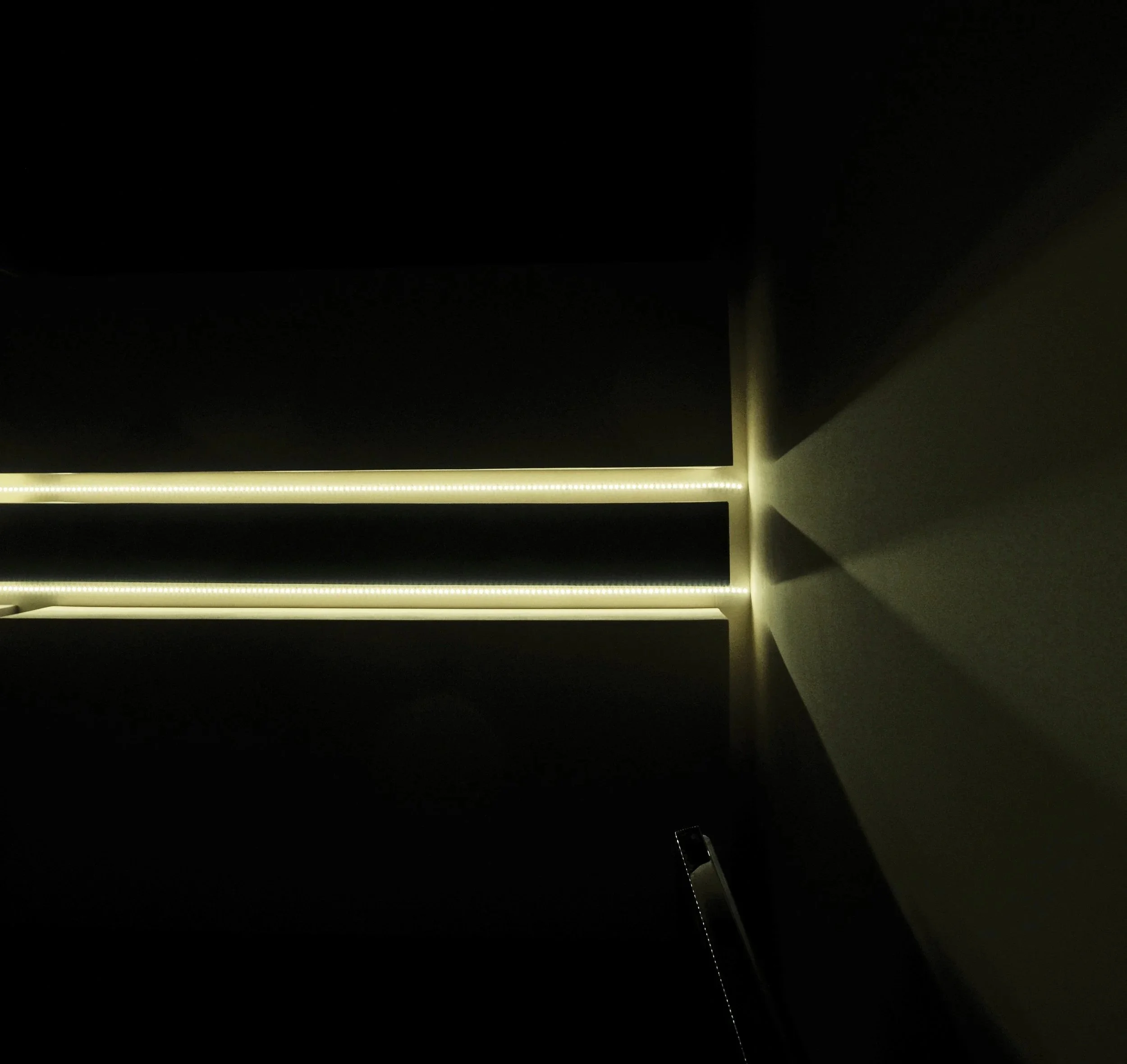 Dark room with a corner illuminated by yellow LED strip lights on the ceiling, casting shadows on the walls.