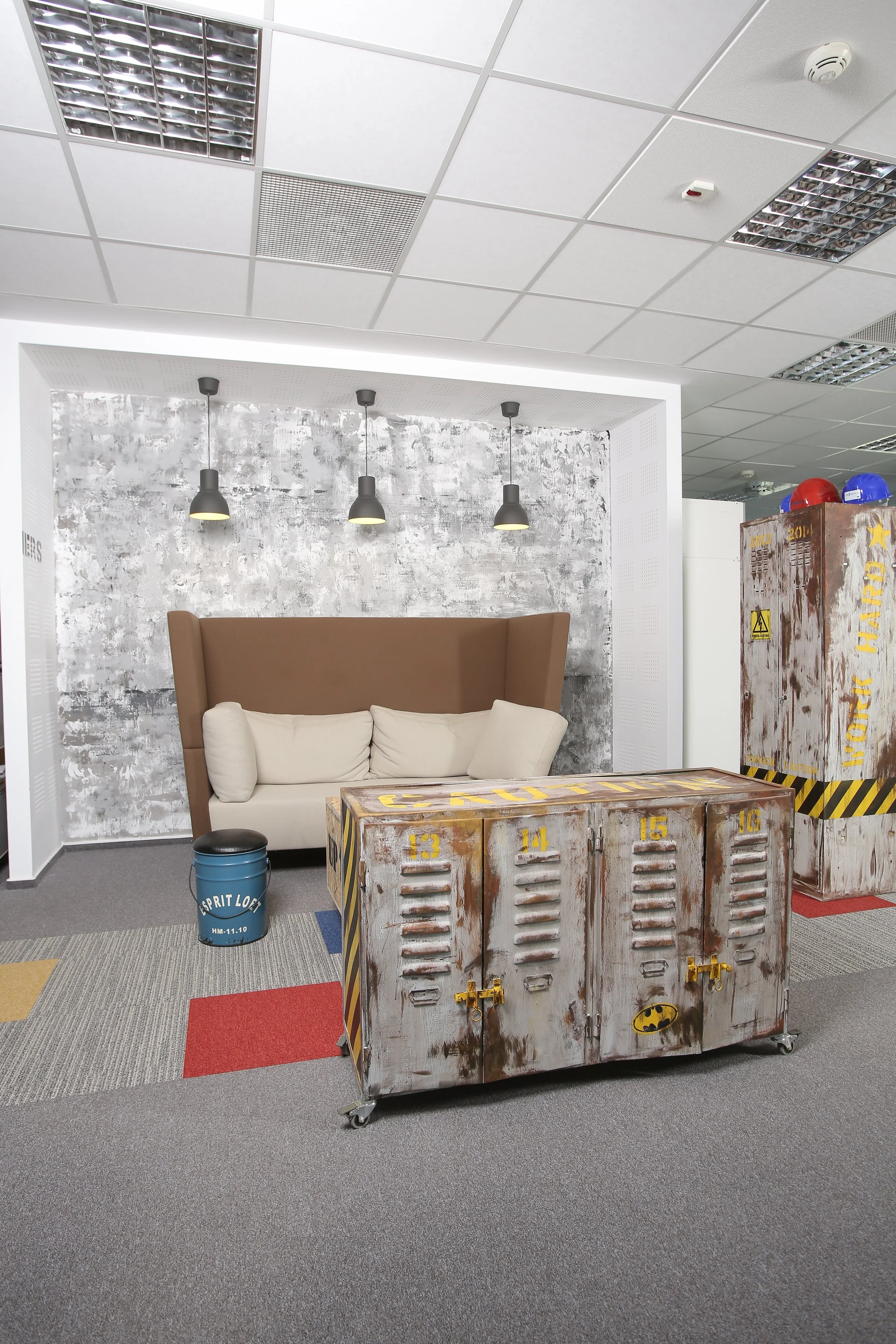 Interior of an office with a beige couch, three black pendant lights, a rustic locker, and a small blue trash can.
