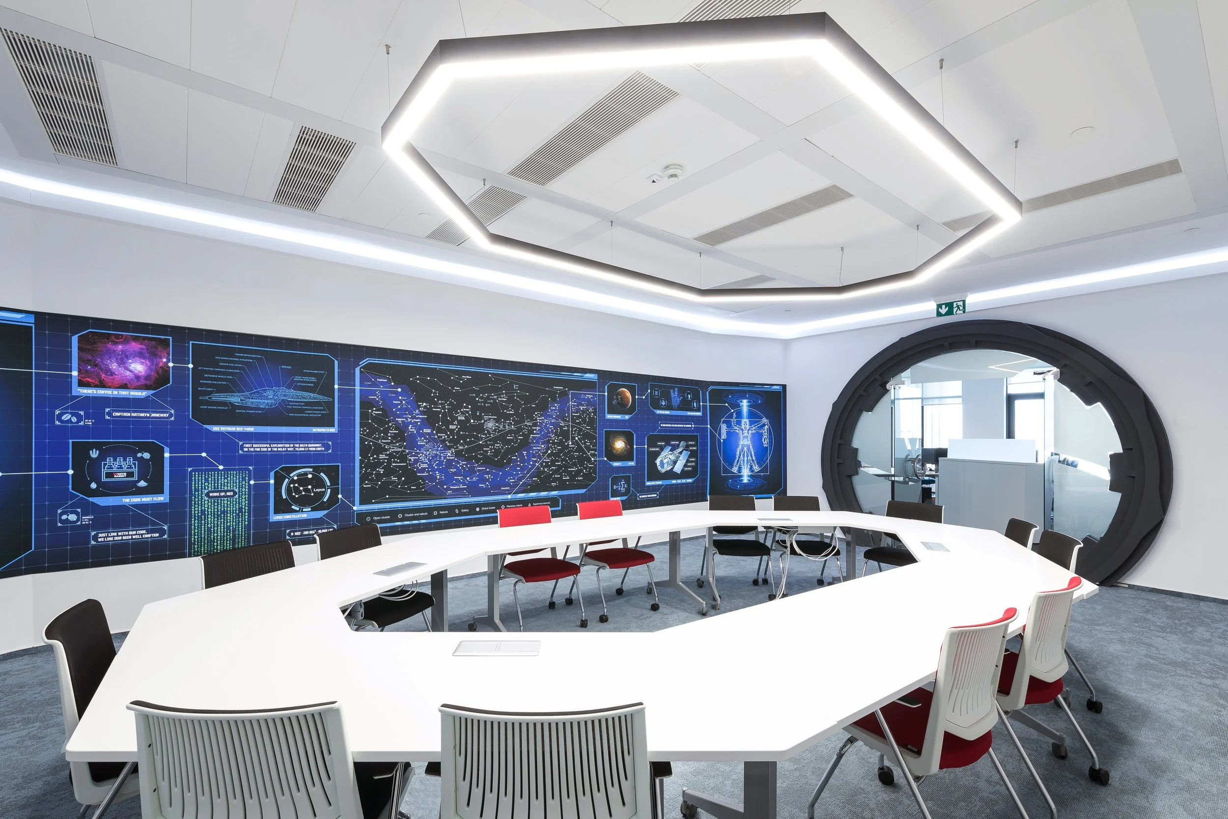 Modern conference room with a large U-shaped white table, chairs, and a digital display wall with space-themed graphics and diagrams.