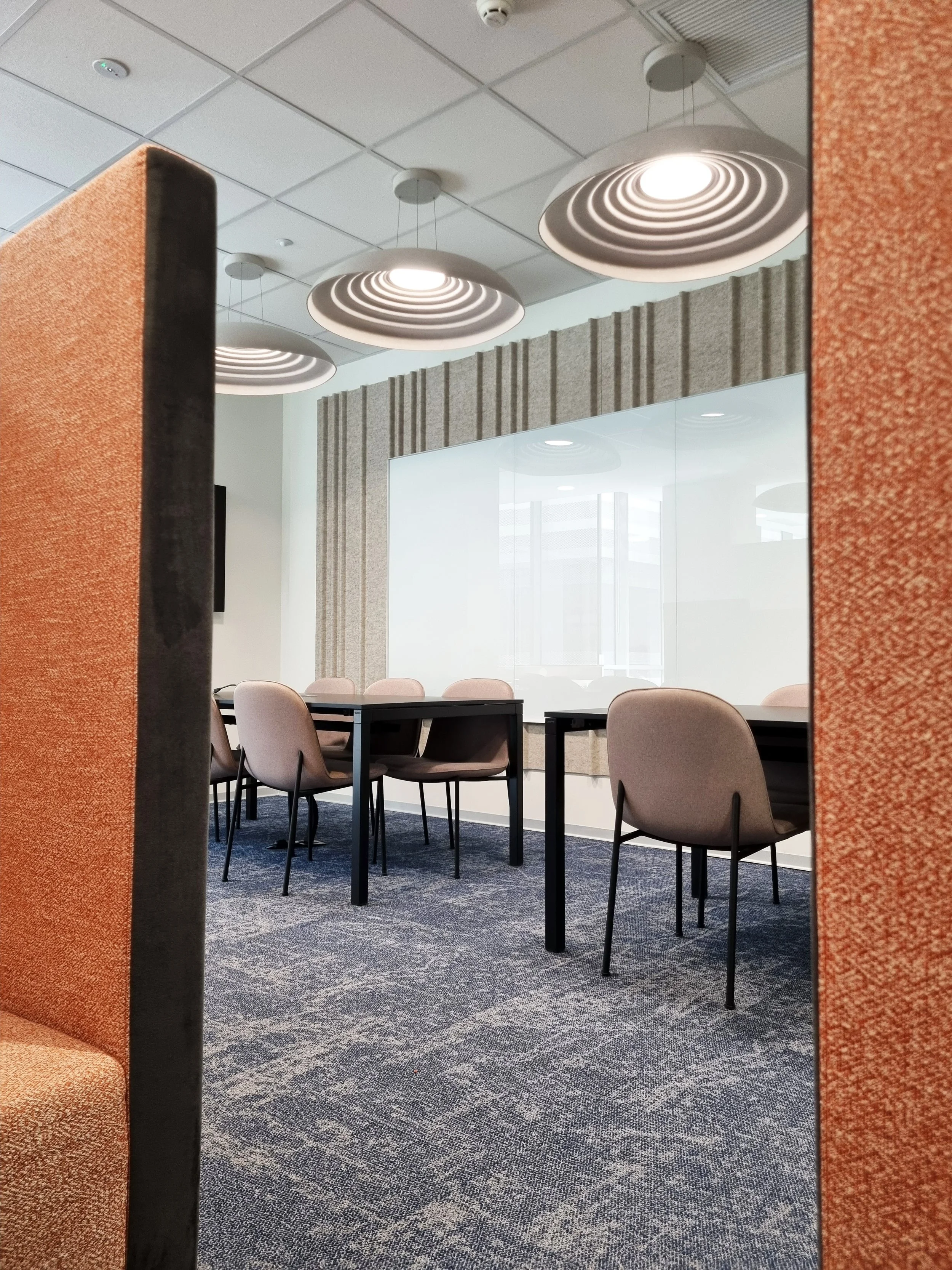 Empty meeting room with beige chairs around black tables, large whiteboard on the wall, and modern ceiling lights.