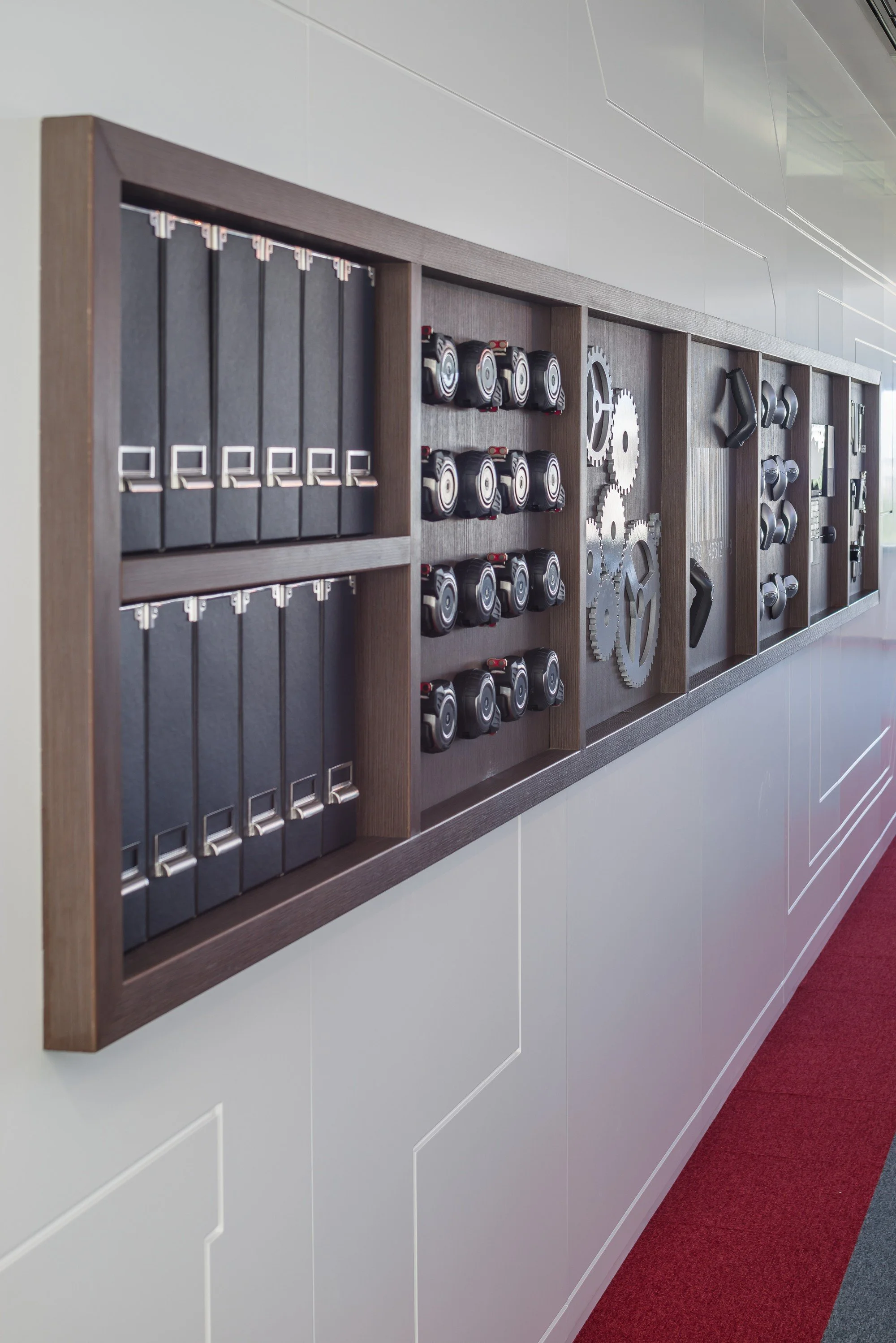 Wall-mounted display with black binders, multiple sets of gears, and various mechanical parts in a modern office.