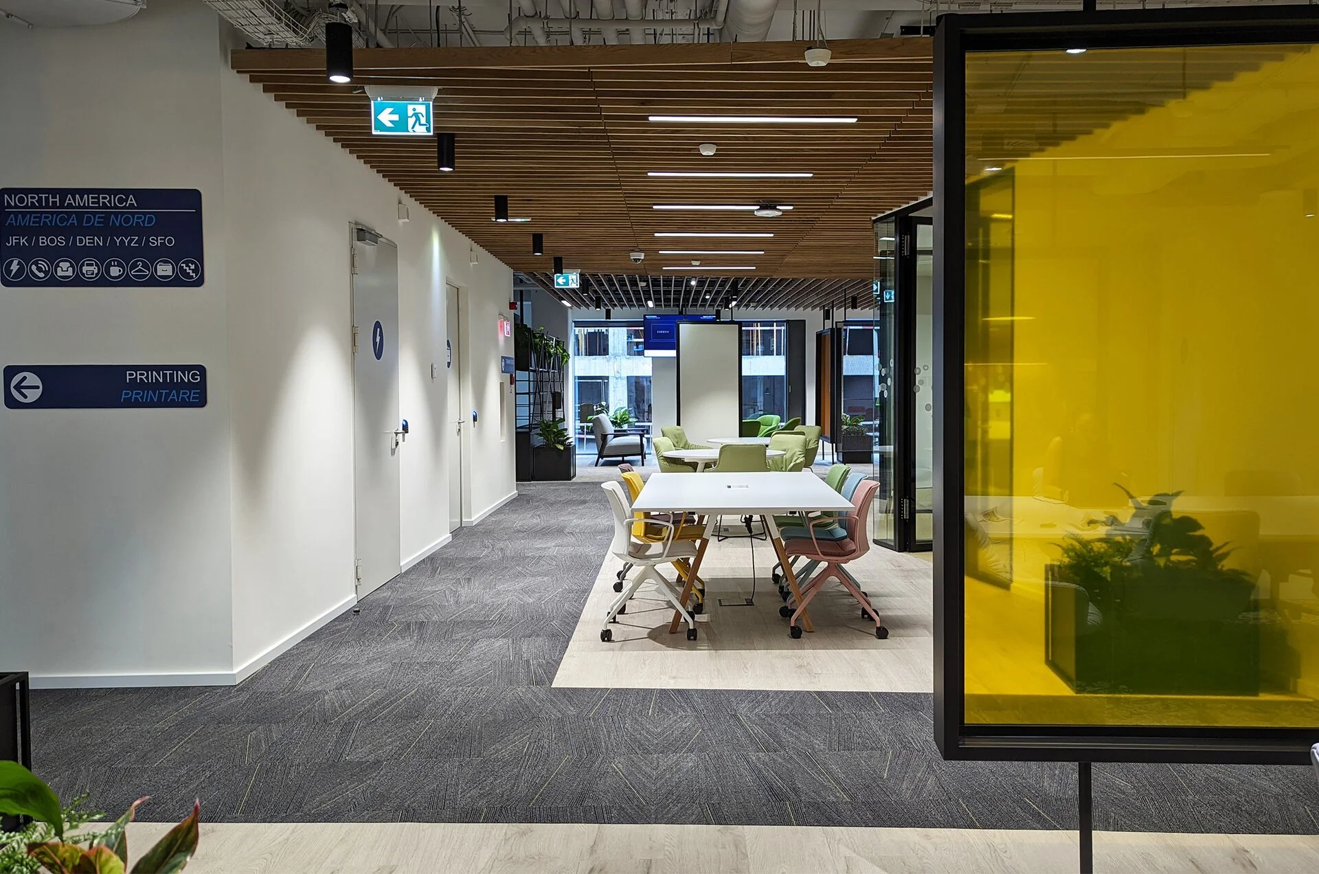 Modern office lounge area with chairs and tables, bright decor, and large windows letting in natural light.
