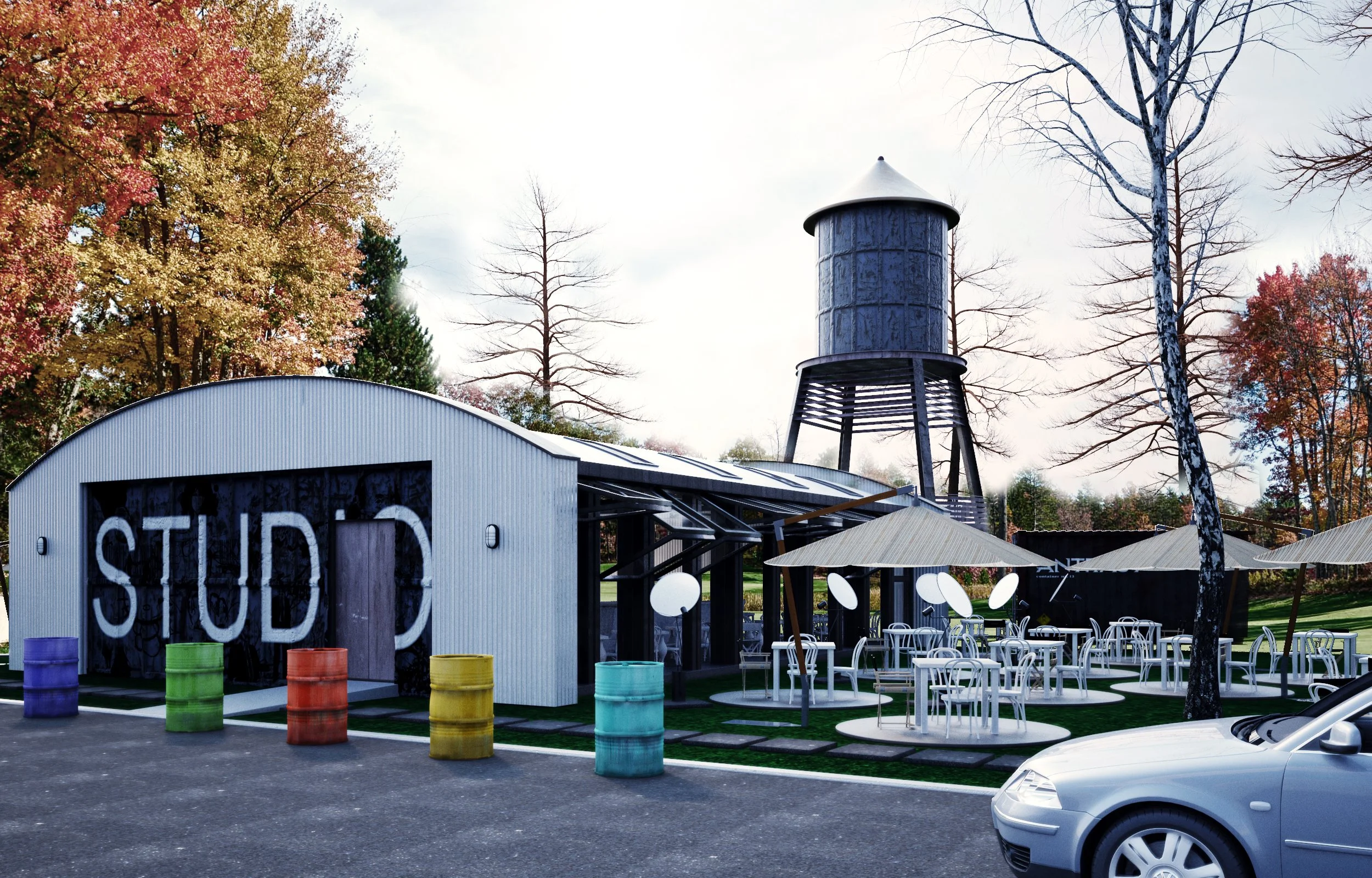 A creative outdoor studio with a white corrugated metal building labeled 'STUDIO', colorful barrels outside, outdoor seating with white chairs and umbrellas, a metal water tower, and trees with autumn leaves.