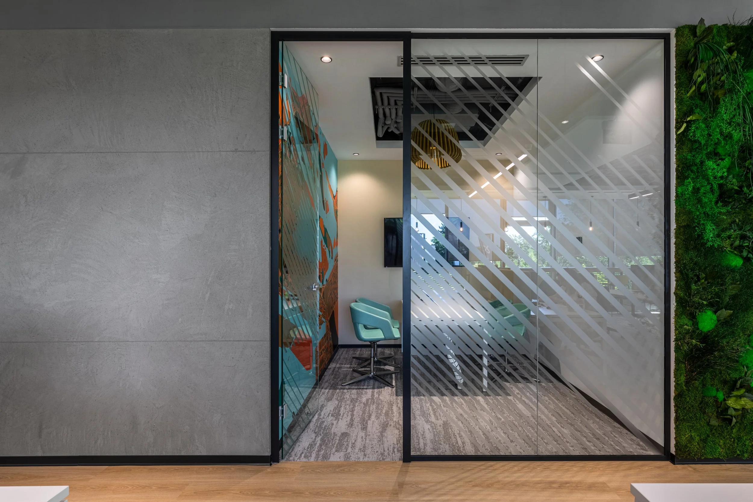 Modern office conference room with glass walls, teal chairs, wall art, and a vertical garden on the side.