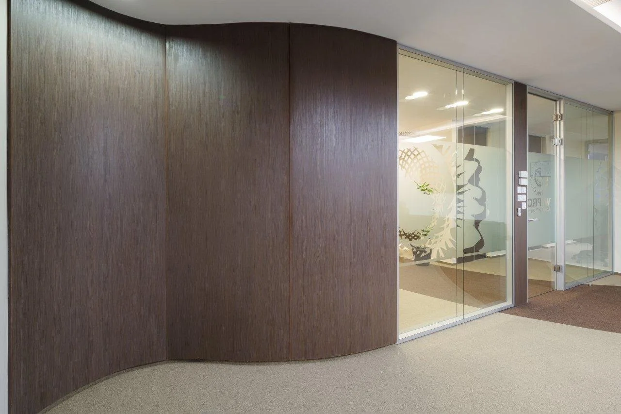 Modern office hallway with a curved wooden wall and glass doors.