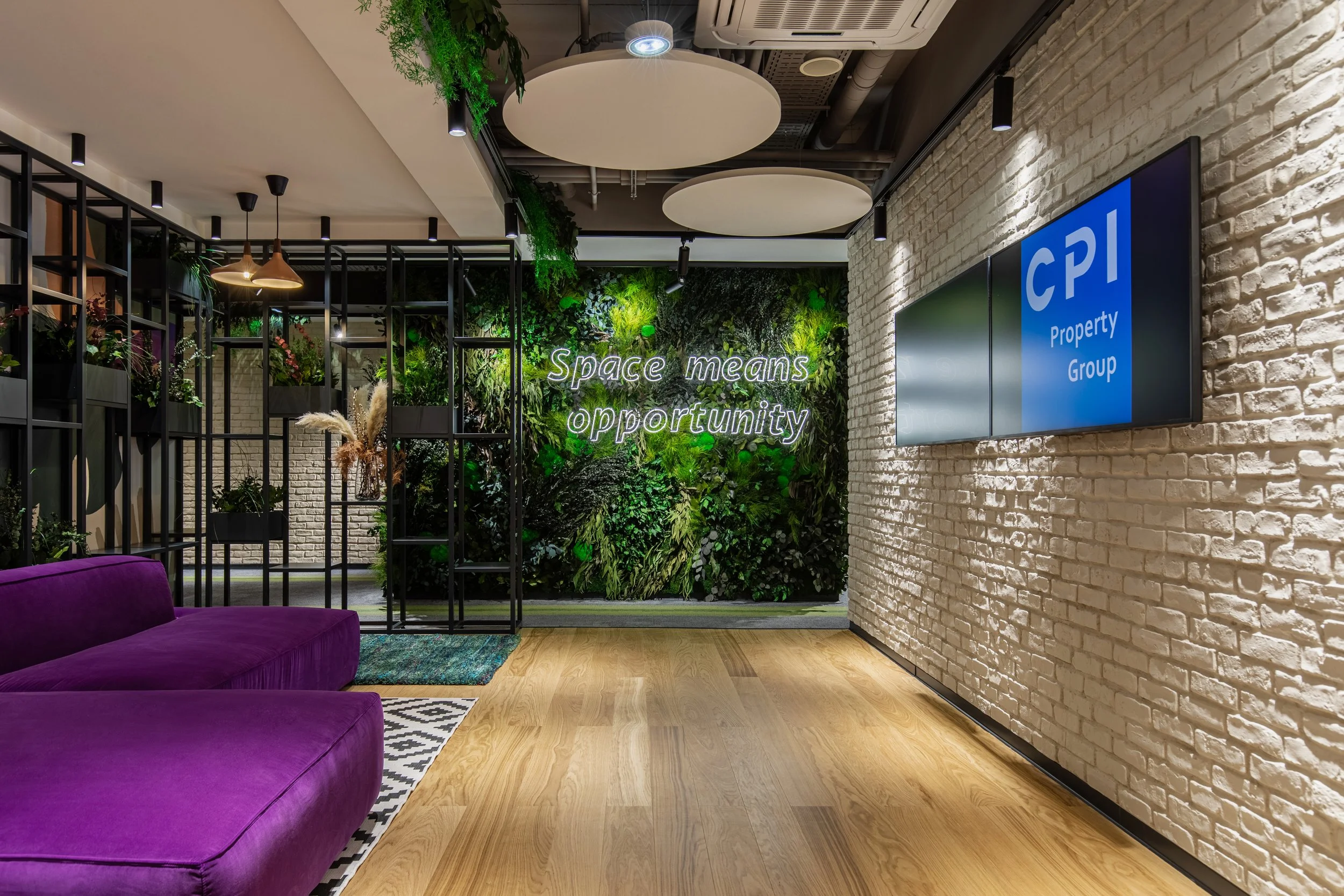 Modern office interior with purple sofa, green wall with plants and neon sign that says 'Space means opportunity', white brick wall with digital screen displaying 'CPI Property Group'