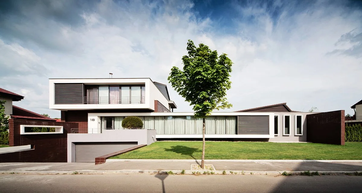 Modern two-story house with white and red brick exterior, large windows, and a green lawn with a single tree in front.