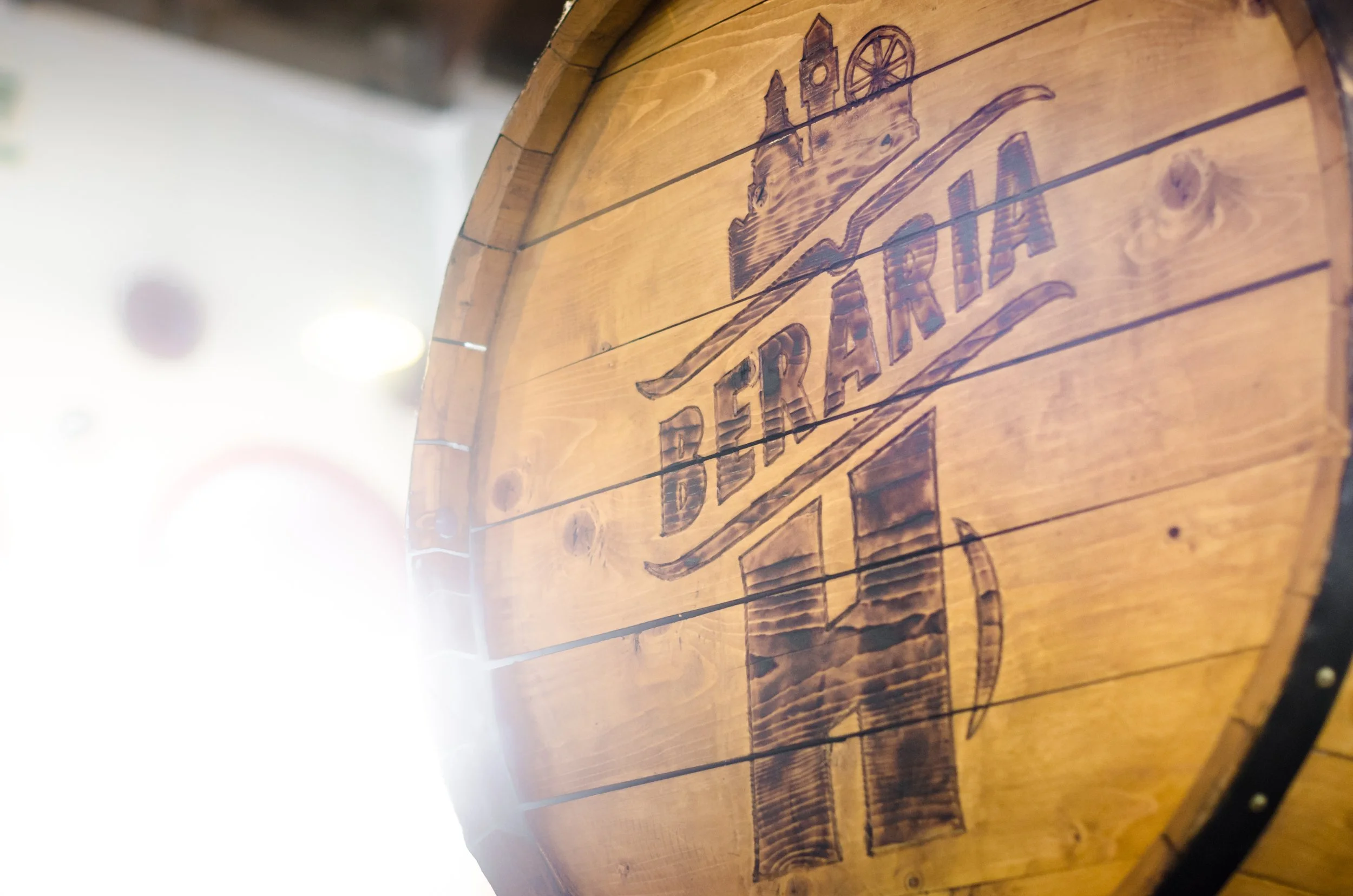 Close-up of a round wooden sign engraved with the words "Trairia Departia" and an illustration of a bottle, a wedge of cheese, and a wine glass.