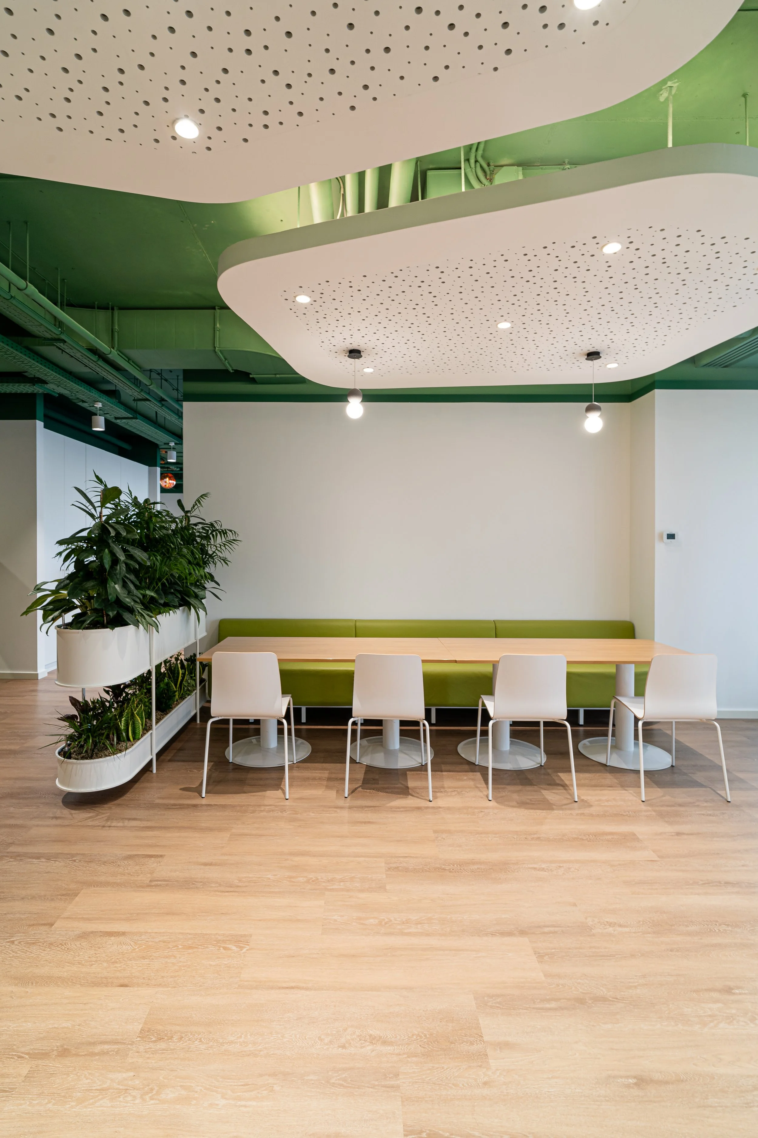 Modern interior with a wooden table, white chairs, a green bench, a plant, and a ceiling with decorative white panels and lighting.