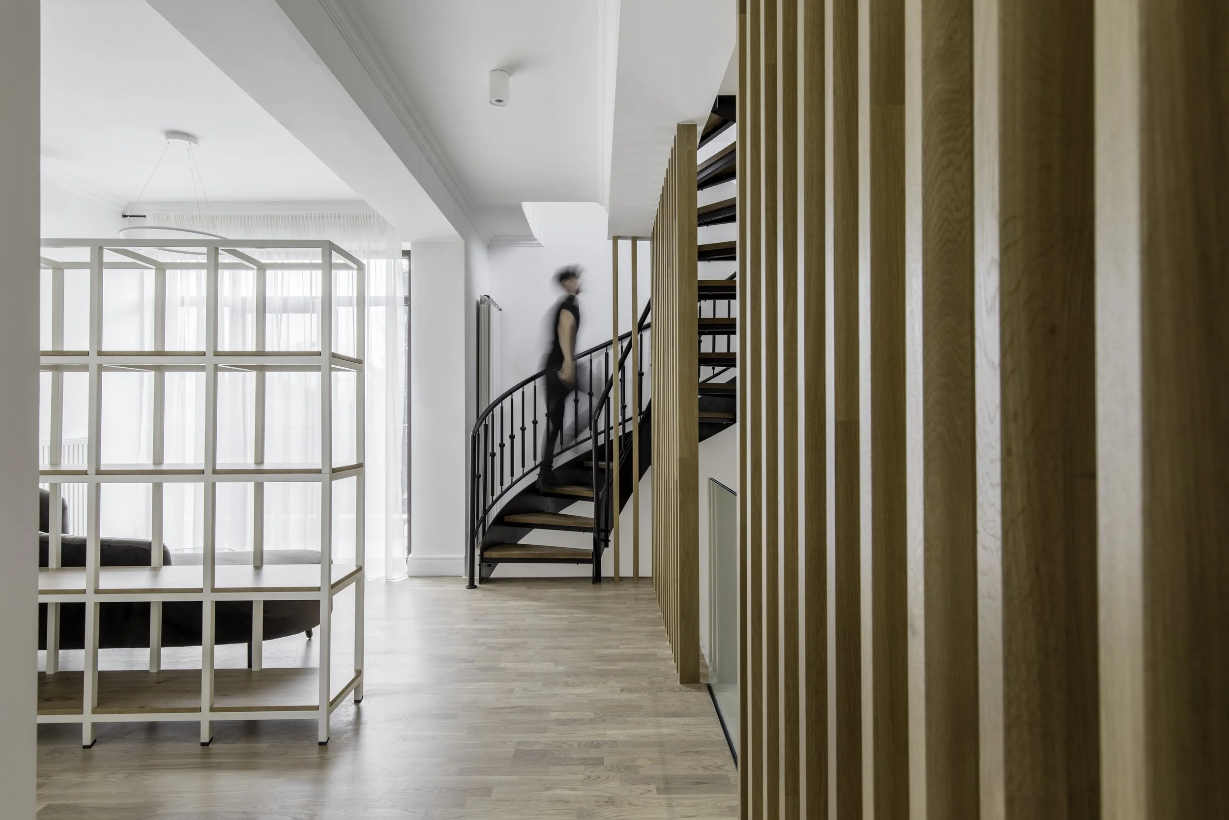 Interior view of a modern, minimalistic living space with a spiral staircase, wooden slat divider, and light wood flooring.