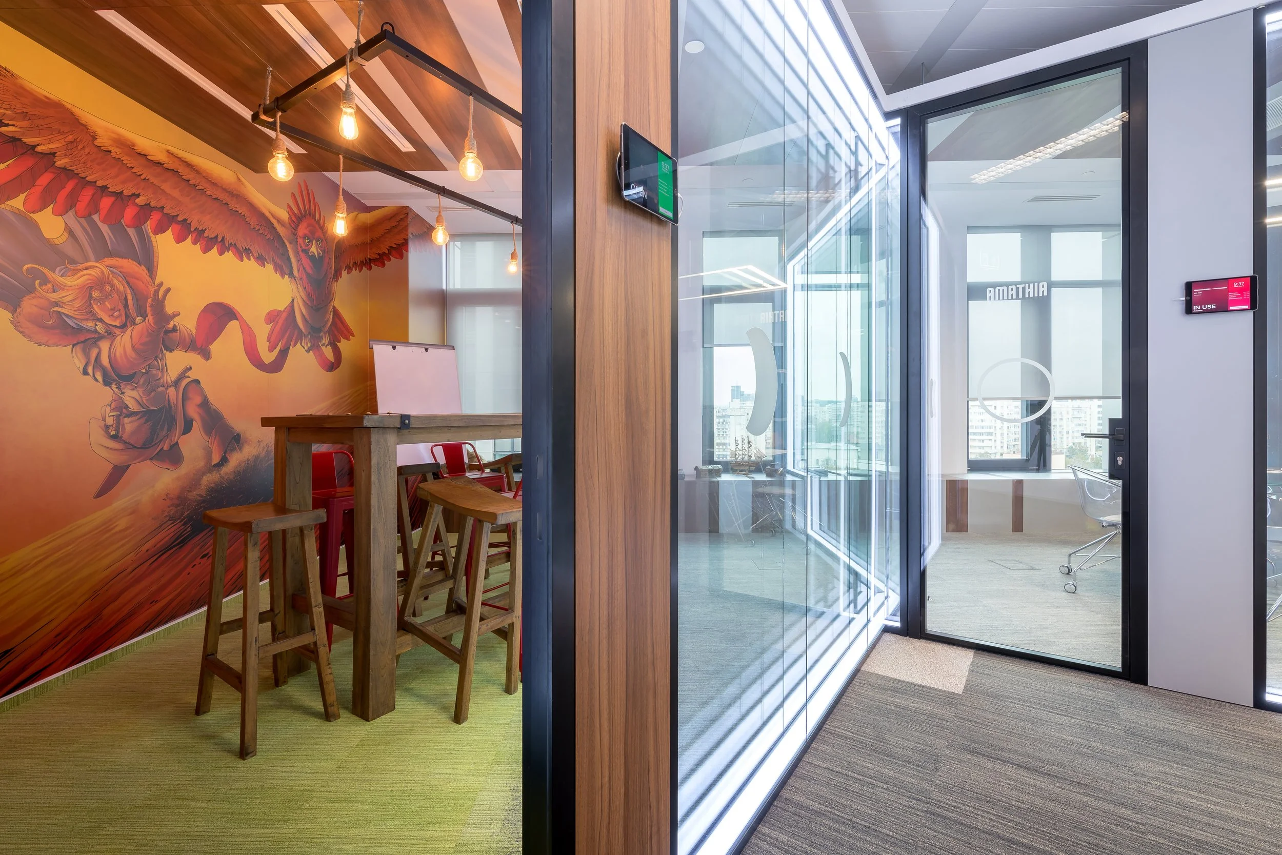 Modern office space with glass walls, a wooden wall, and a colorful mural of a girl flying with a winged cat, illuminated by hanging light bulbs.