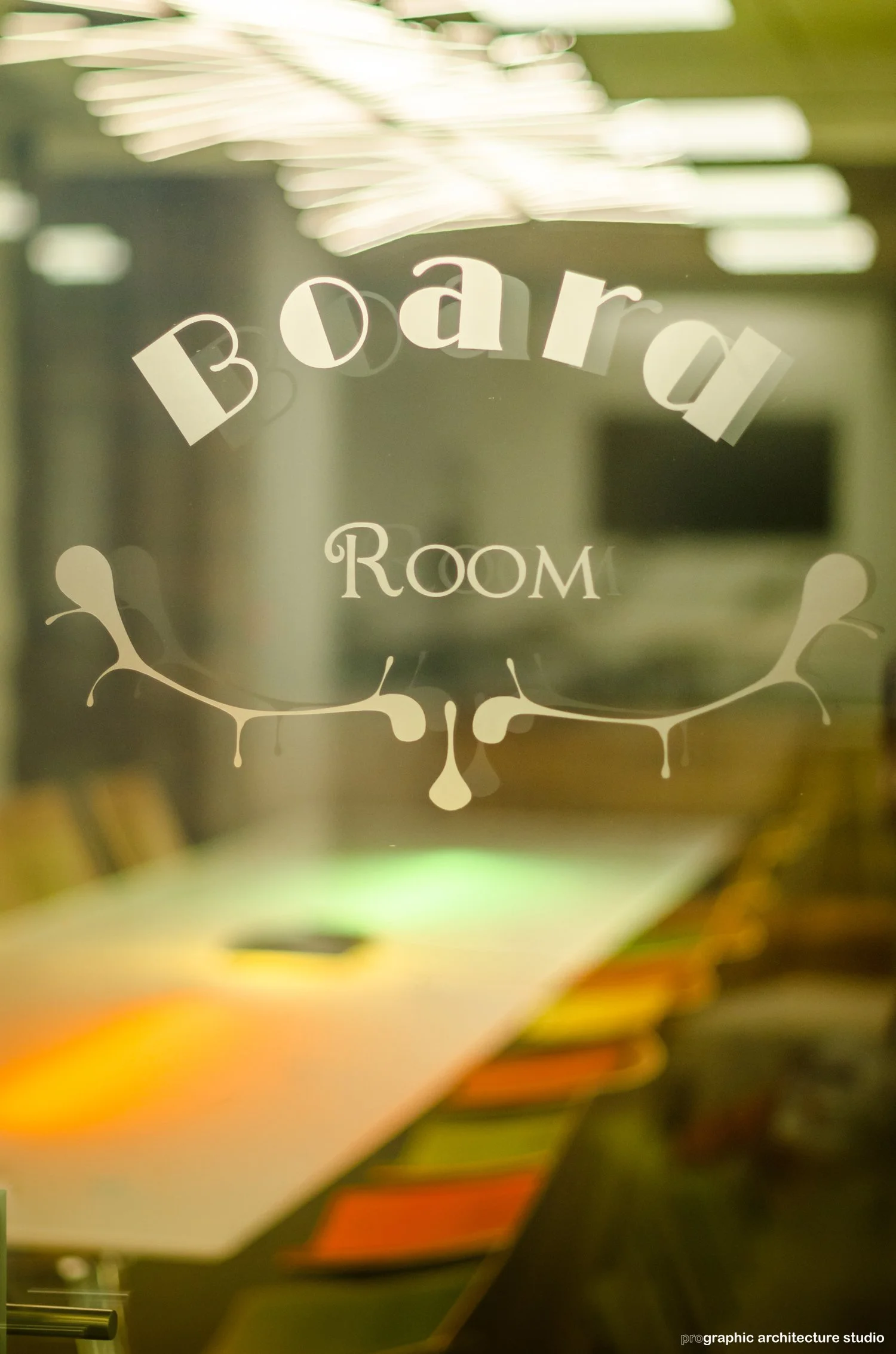 A glass door with text that reads 'Board Room' and decorative design underneath, reflecting an office environment.