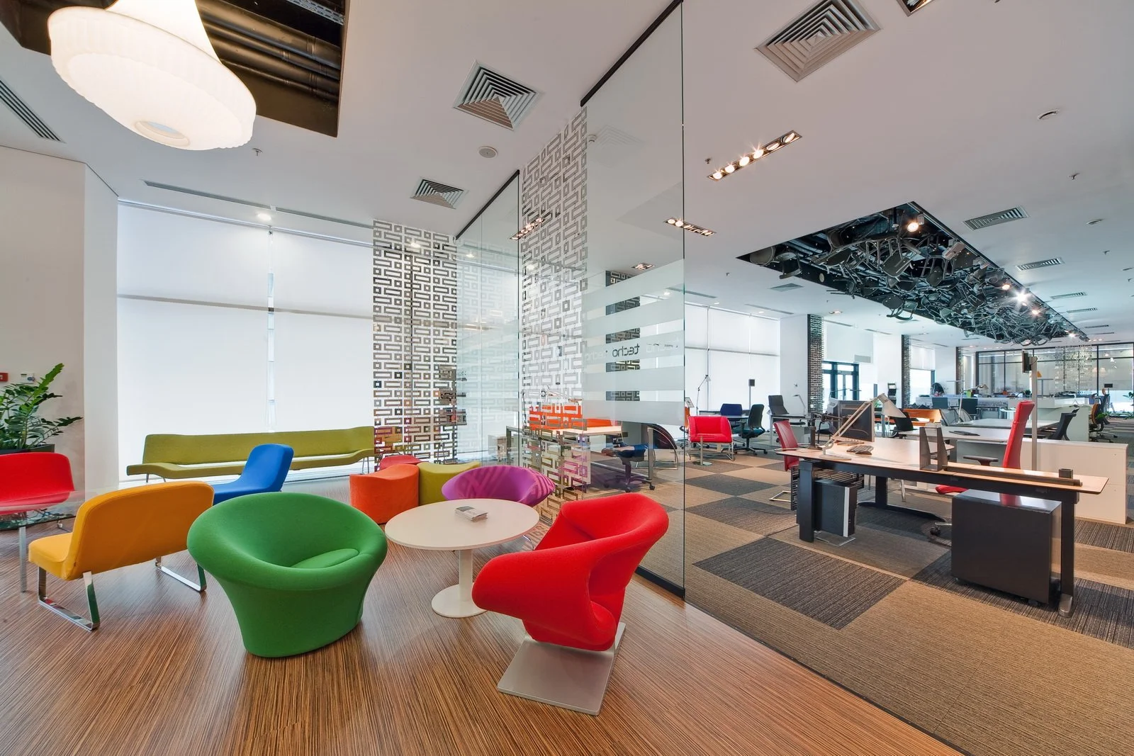 Modern office space with colorful chairs, a round white table, and open workstations with red and black chairs.