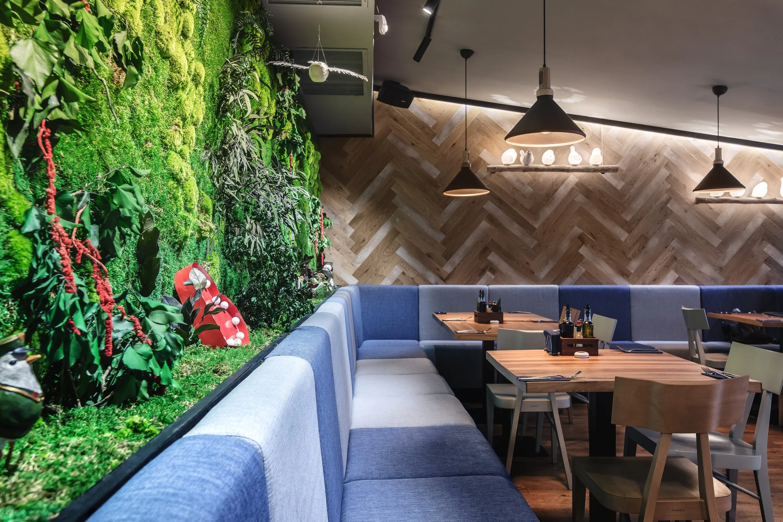 Interior of a restaurant with a green wall, wooden tables, and chairs, decorated with hanging pendant lights.