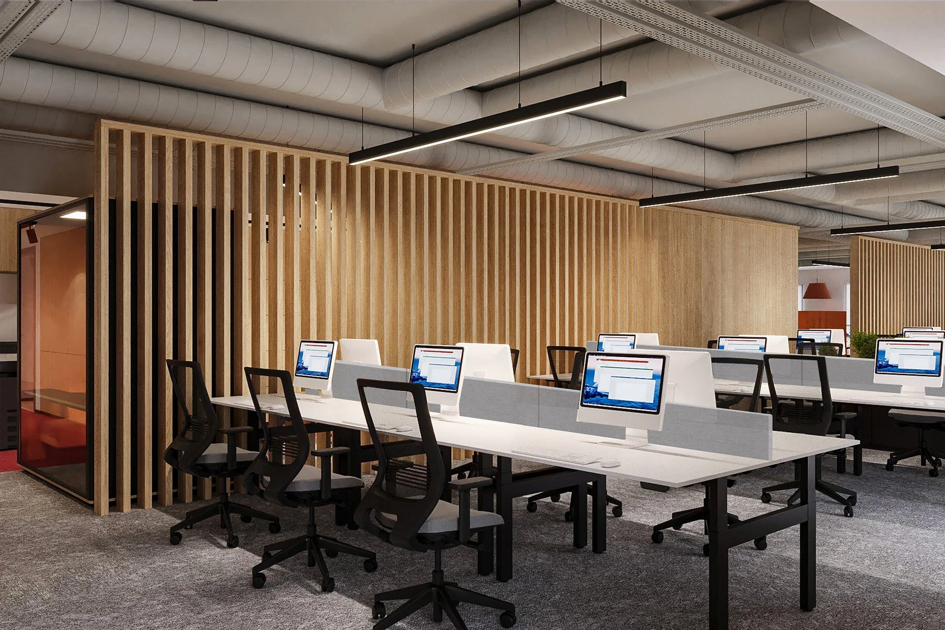 Modern office workspace with multiple desks, computer monitors, black office chairs, wooden wall partition, and exposed duct ceiling.