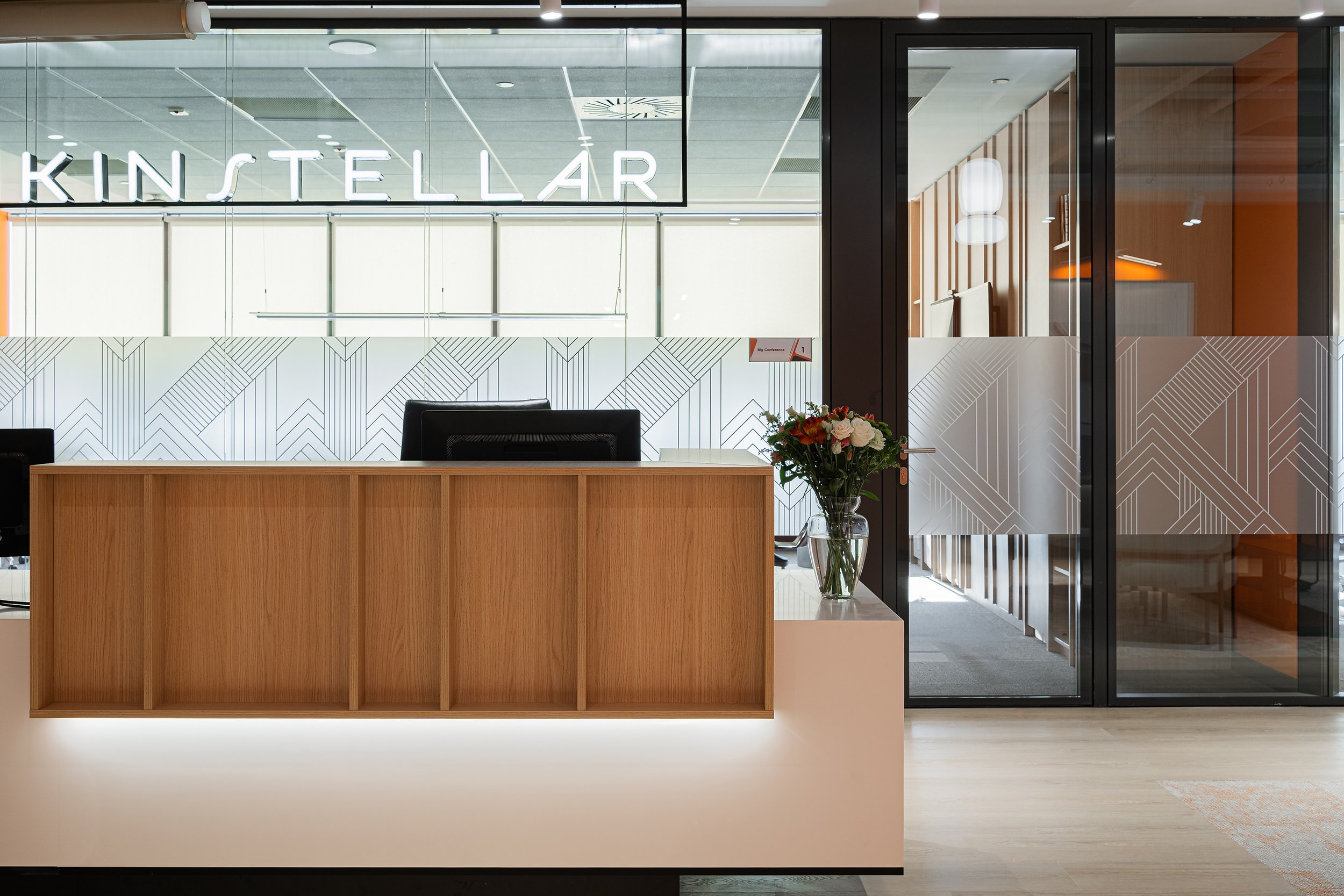 Modern office reception desk with a bouquet of flowers, glass door behind with frosted design illuminated sign.