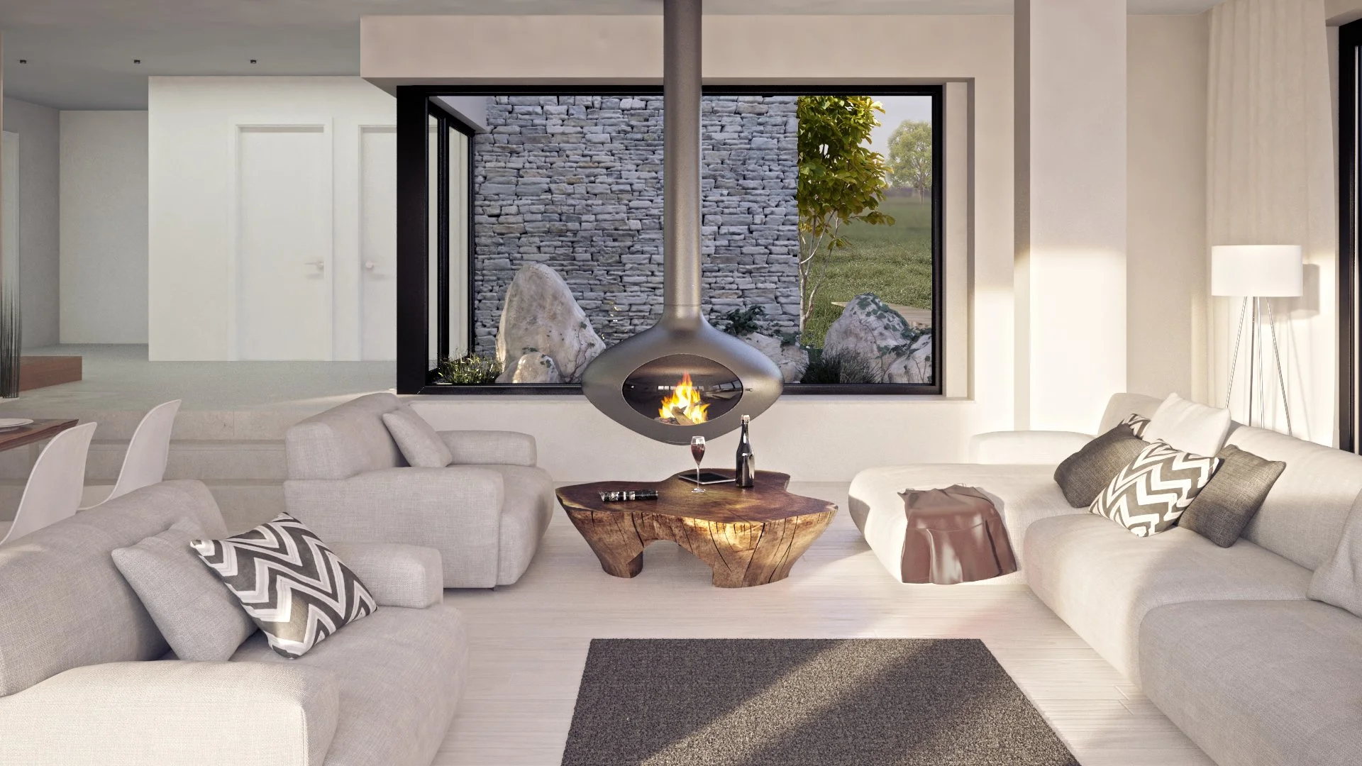 Modern living room with beige sofas, decorative pillows, a wooden coffee table, and a fireplace with a hanging chimney. Large window showing a stone wall, rocks, and greenery outside.