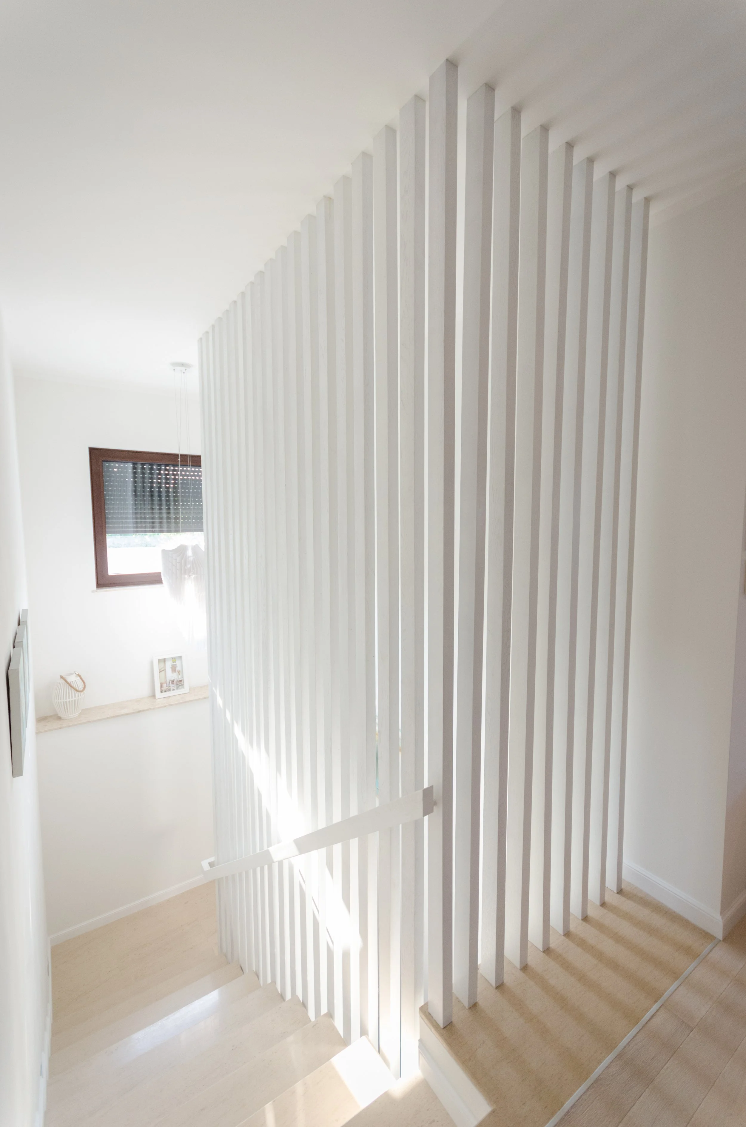 Interior view of a staircase with white vertical slats and a handrail, with a window letting in natural light.
