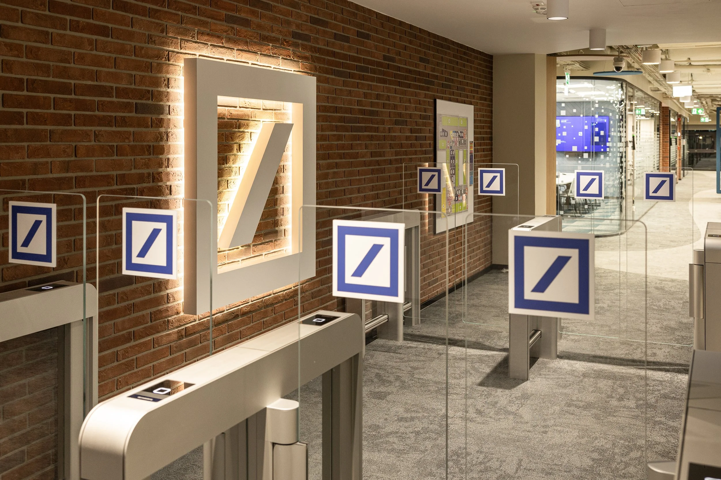 Empty Siemens turnstiles in an office lobby with brick wall, Siemens logo on a illuminated square, glass doors, and digital screens in the background.