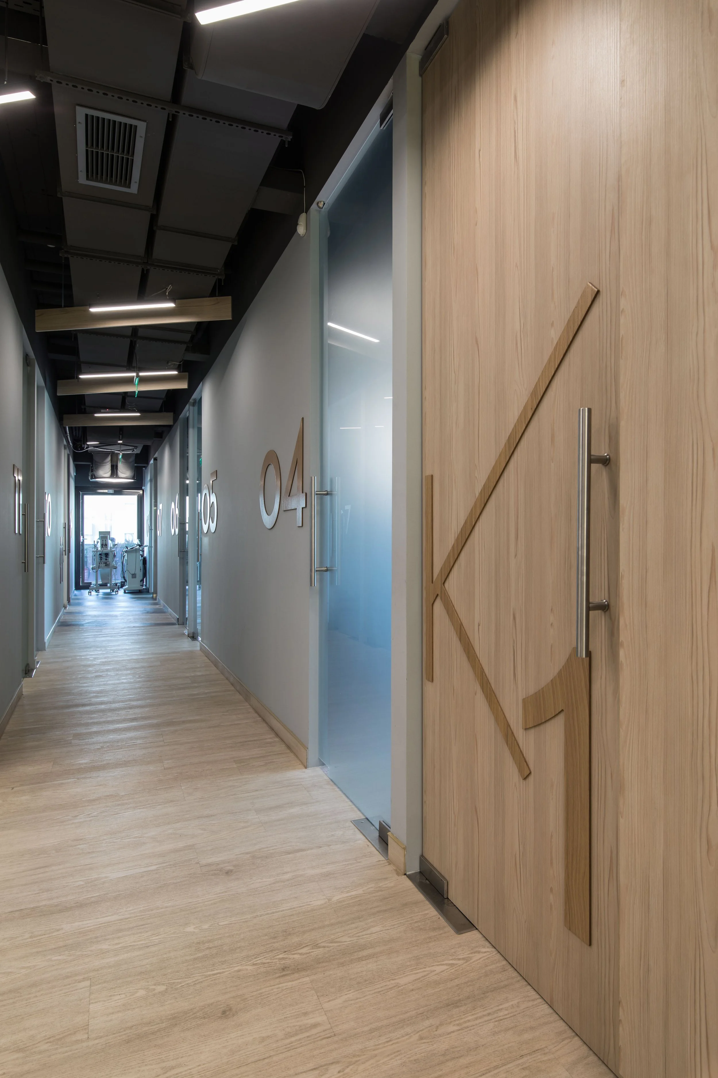 Modern hallway with wooden floors and doors, numbered 04 and 05, with minimalist decor and ceiling lighting, leading to a bright exit.