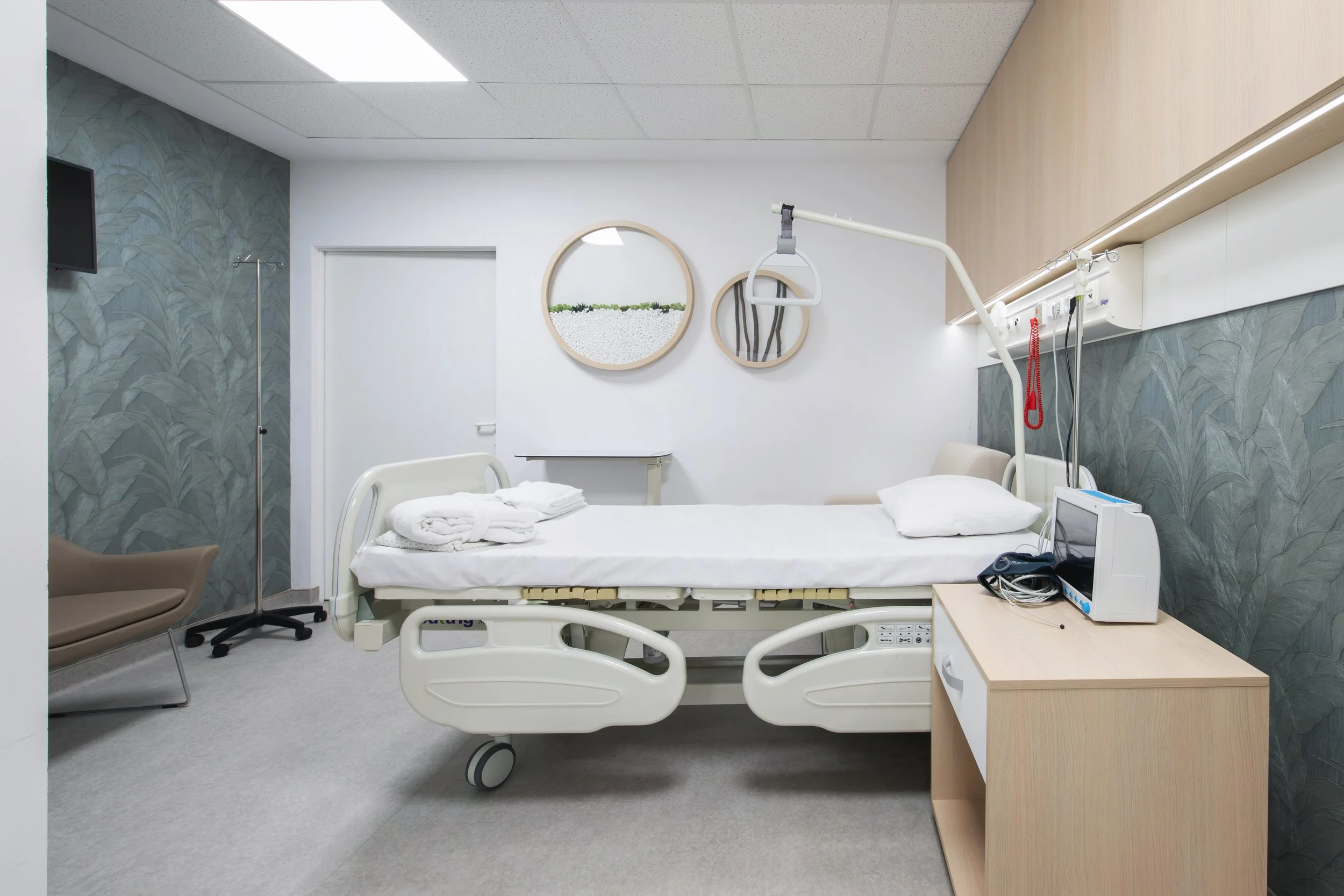 Modern hospital room with adjustable bed, pillow, towels, medical equipment, and decorative wall art.